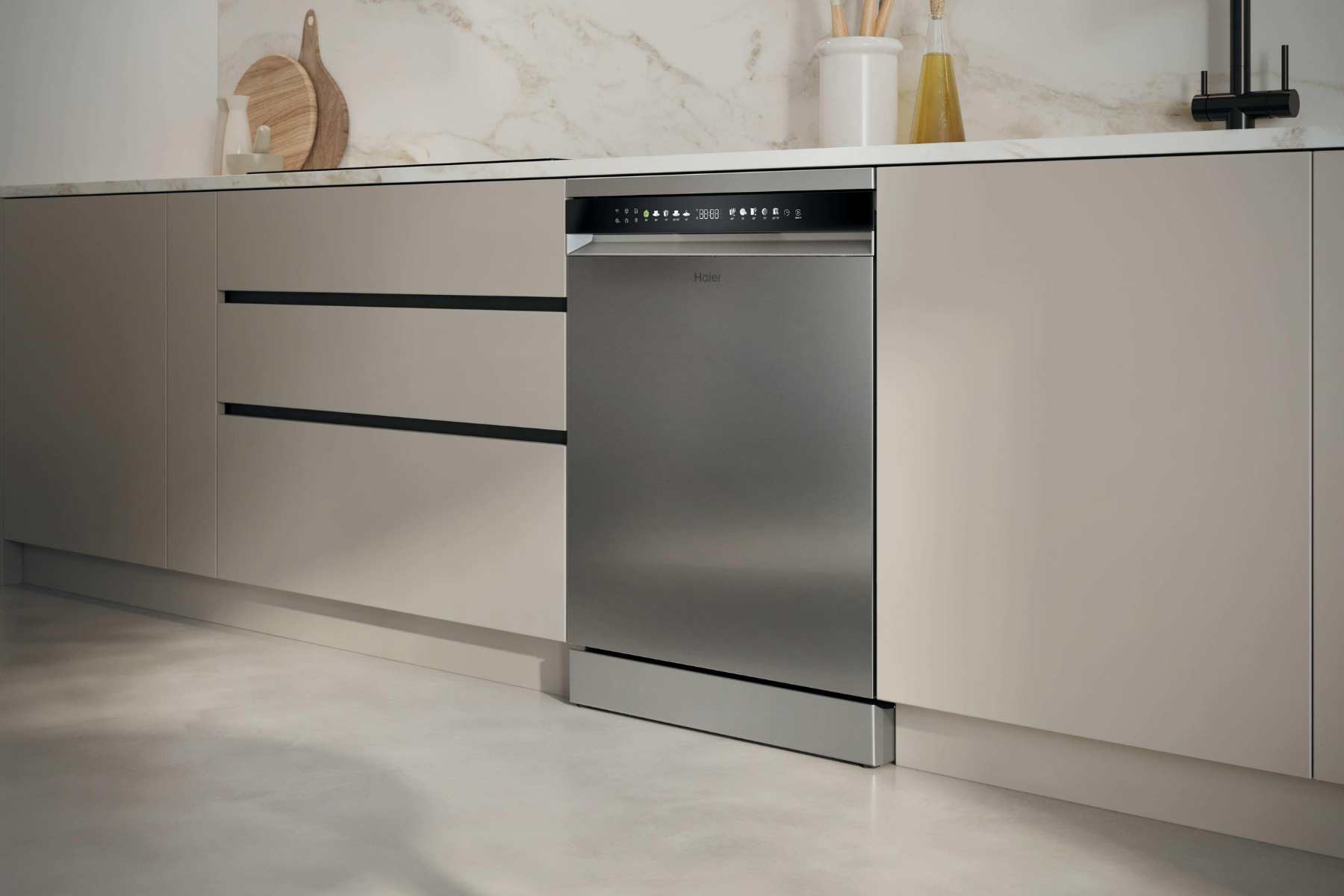 Un lavavajillas Haier de acero inoxidable instalado bajo una encimera de mármol blanco en una cocina moderna con armarios beiges.