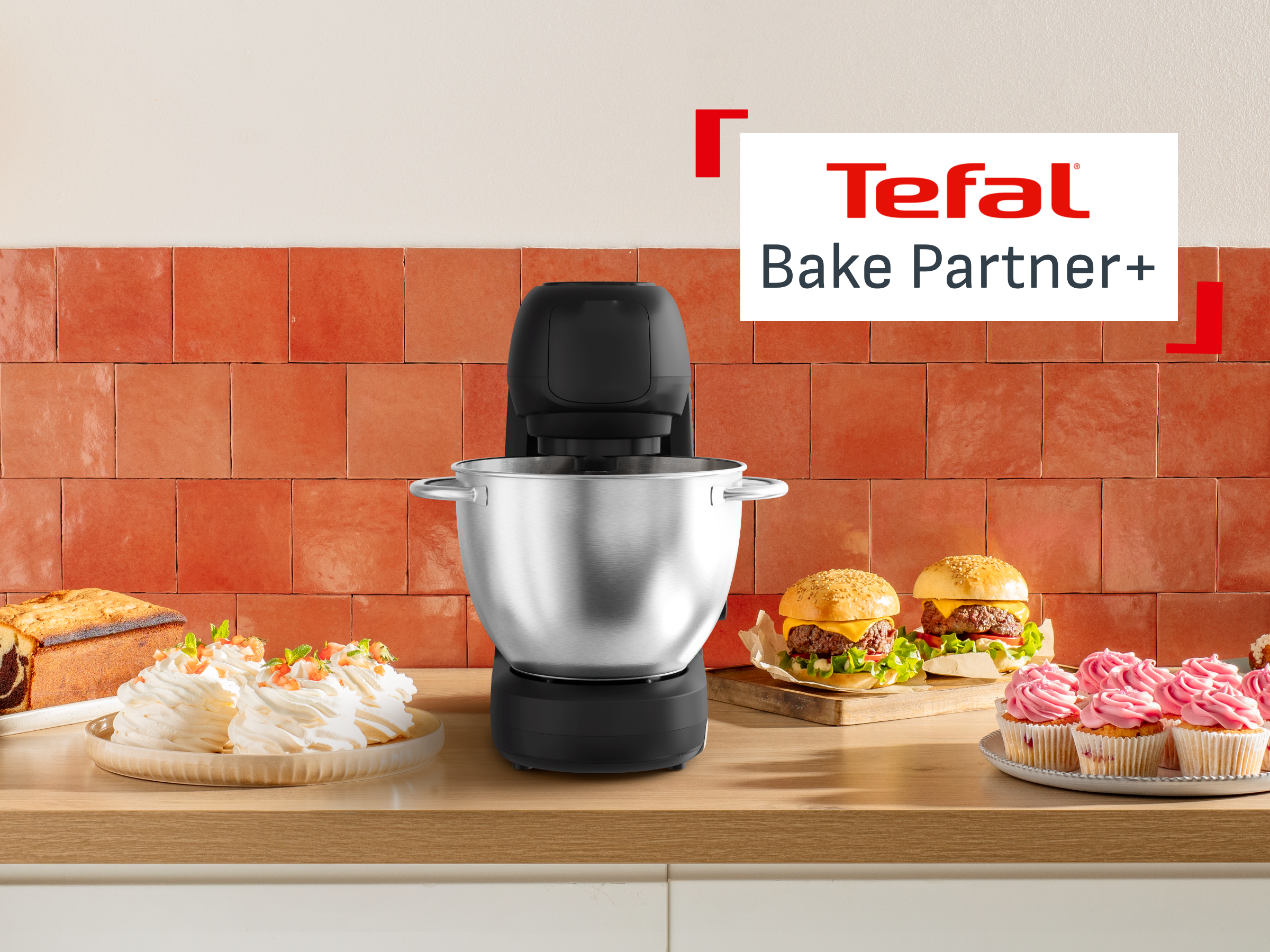 Egy fekete Tefal Bake Partner+ álló mixer egy pulton, süteményekkel és burgerekkel körülvéve.