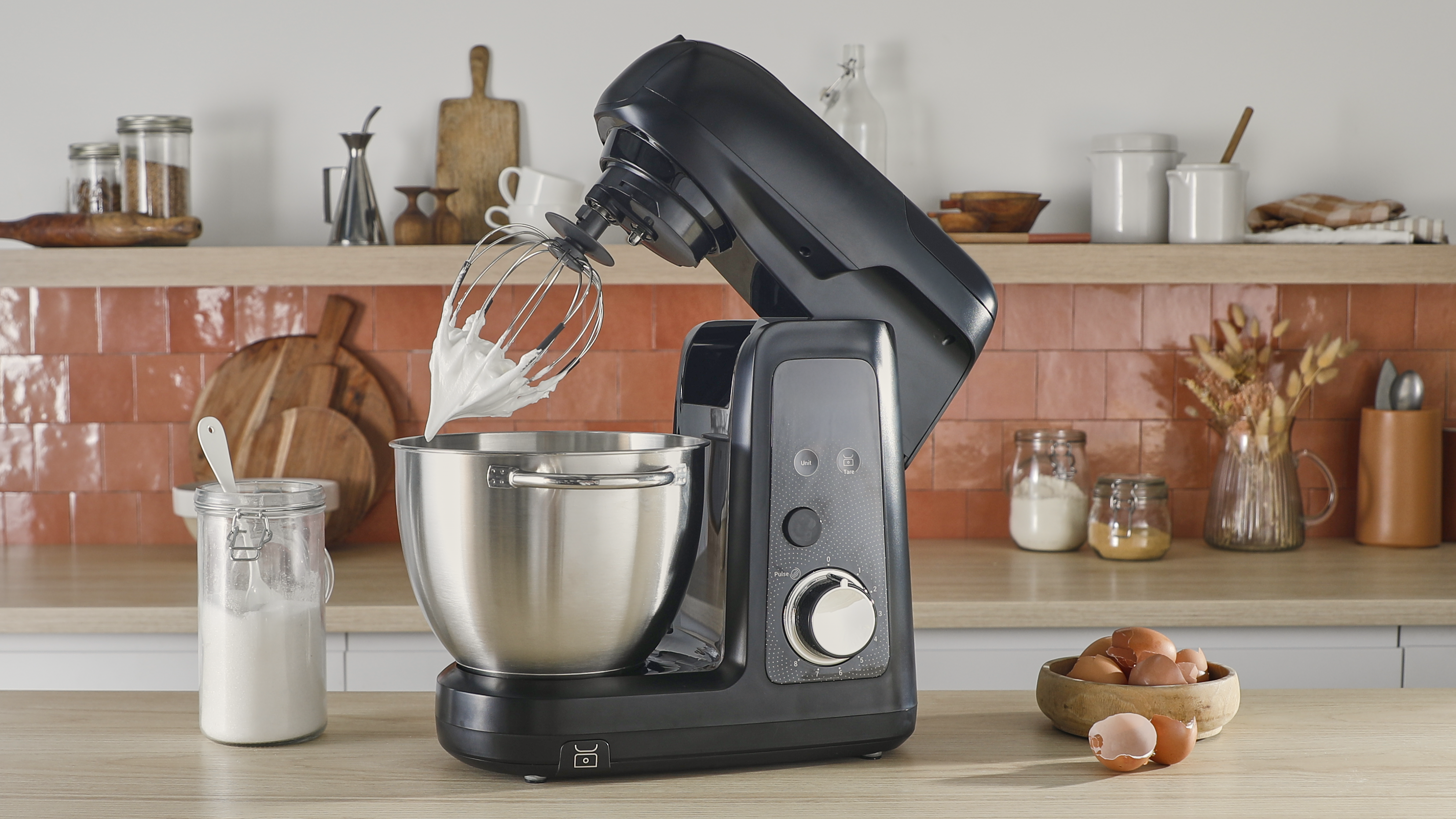 Egy fekete álló mixer rozsdamentes acél tálal egy fa konyhapulton.