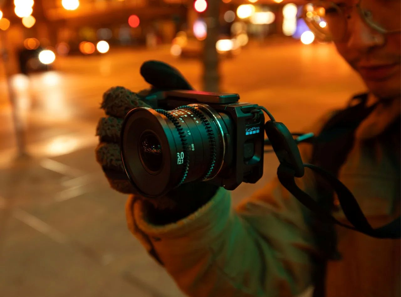 Person hält eine modifizierte GoPro-Kamera mit großem Objektiv bei Nacht vor einer Stadtkulisse.