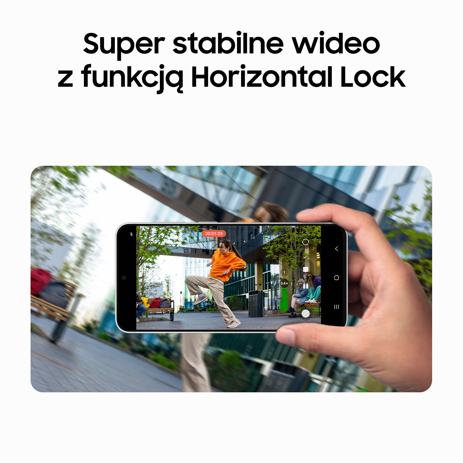 Ręka trzyma smartfon pokazujący stabilne wideo tańczącej na zewnątrz osoby.