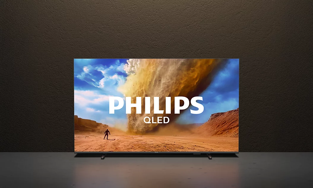 Koyu renkli bir duvar önündeki masada duran Philips QLED televizyonda tozlu bir çöl manzarası görünüyor.