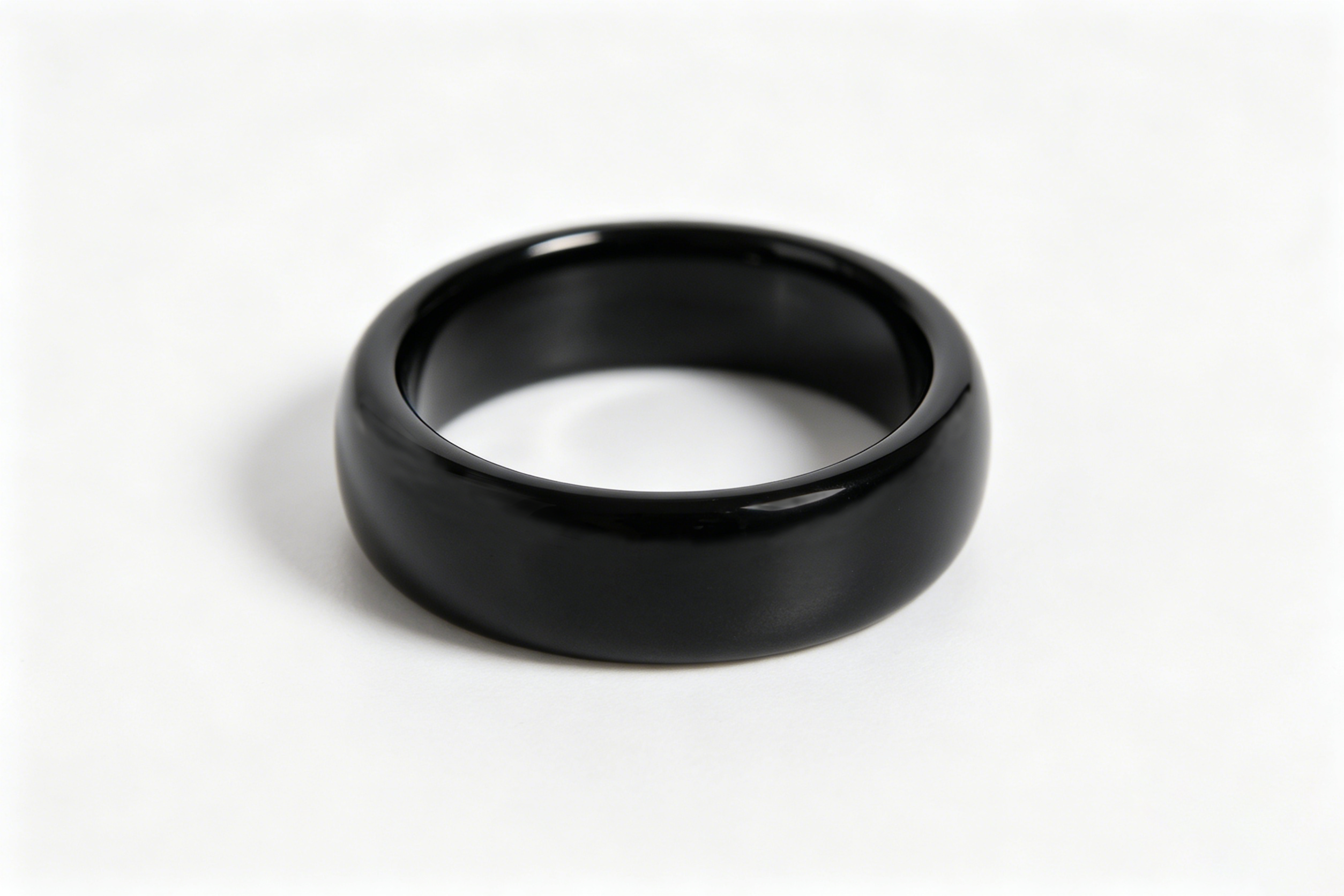 Une bague noire et brillante repose sur une surface claire.