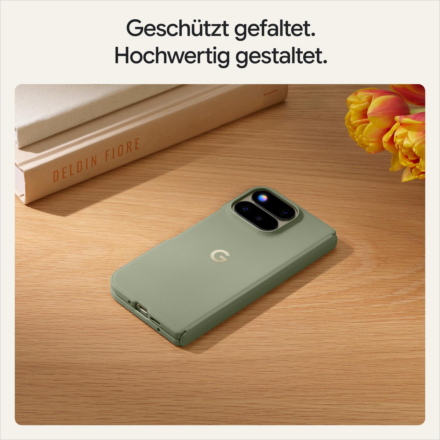 Ein grünes faltbares Smartphone liegt auf einem Holztisch, daneben Bücher und gelbe Tulpen.