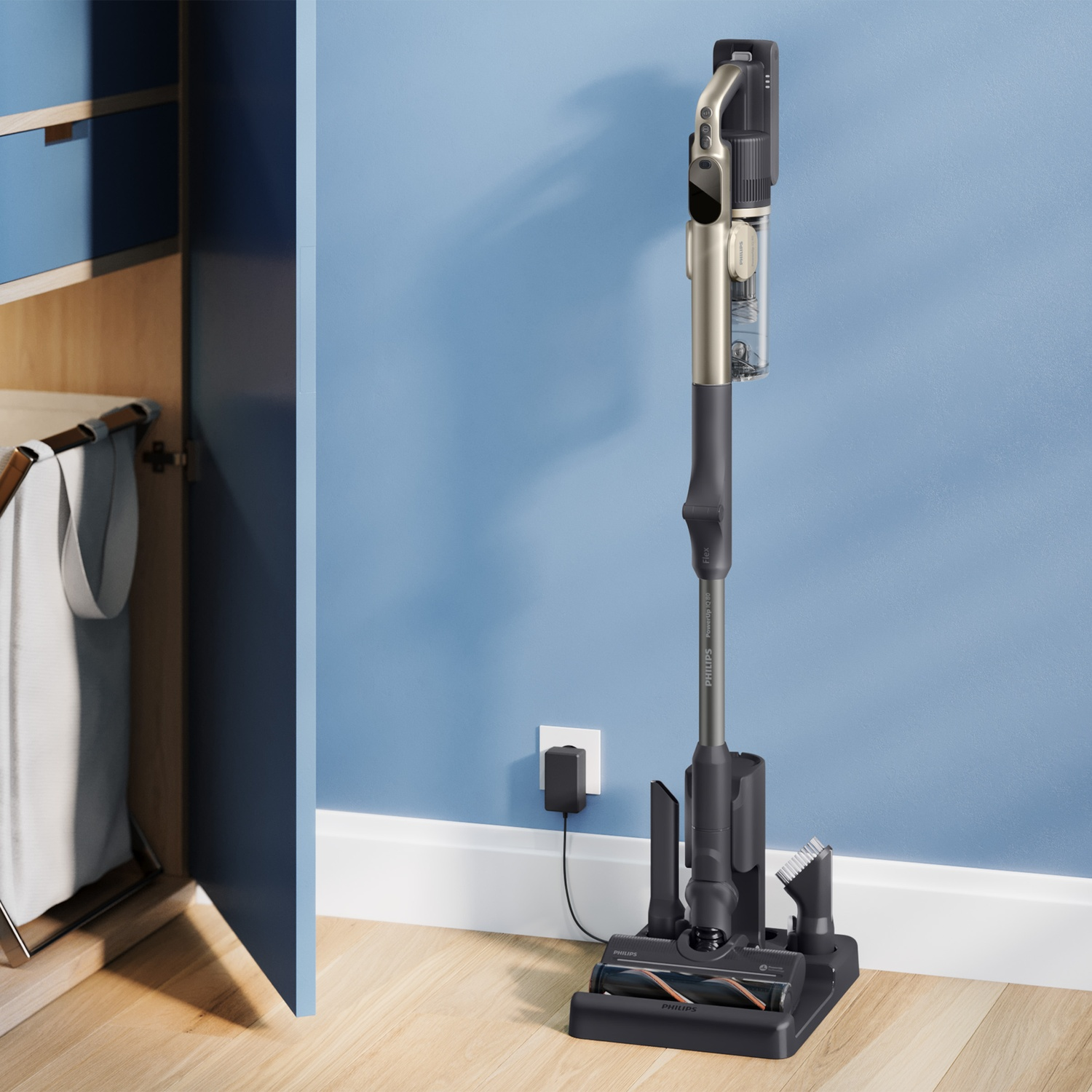 A grey cordless vacuum cleaner stands on a charging dock against a blue wall.