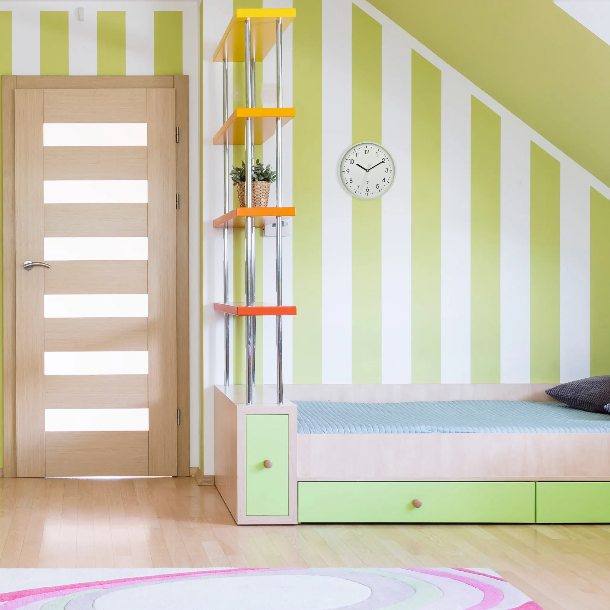 Ein Zimmer mit grün-weiß gestreiften Wänden, einem Holzbett, bunten Regalen und einer Holztür.
