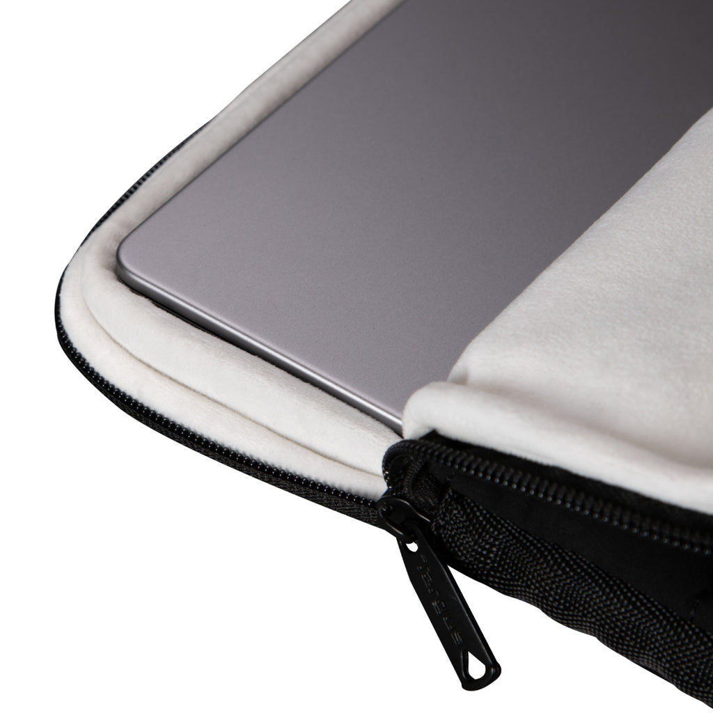 Una laptop plateada descansa dentro de una funda protectora acolchada en blanco y negro con cremallera.