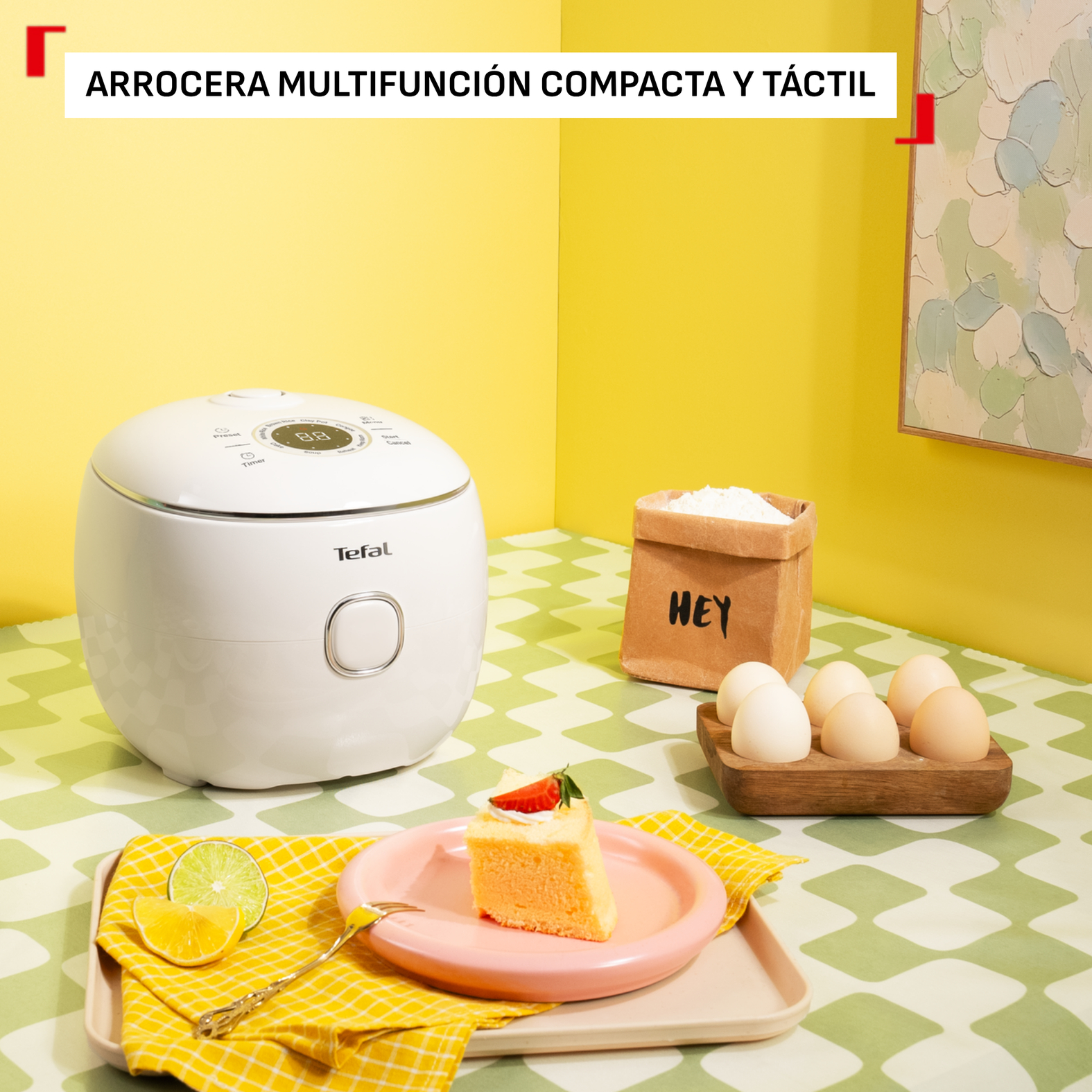 Una arrocera Tefal blanca sobre una mesa de cuadros verdes con pastel, huevos y harina.