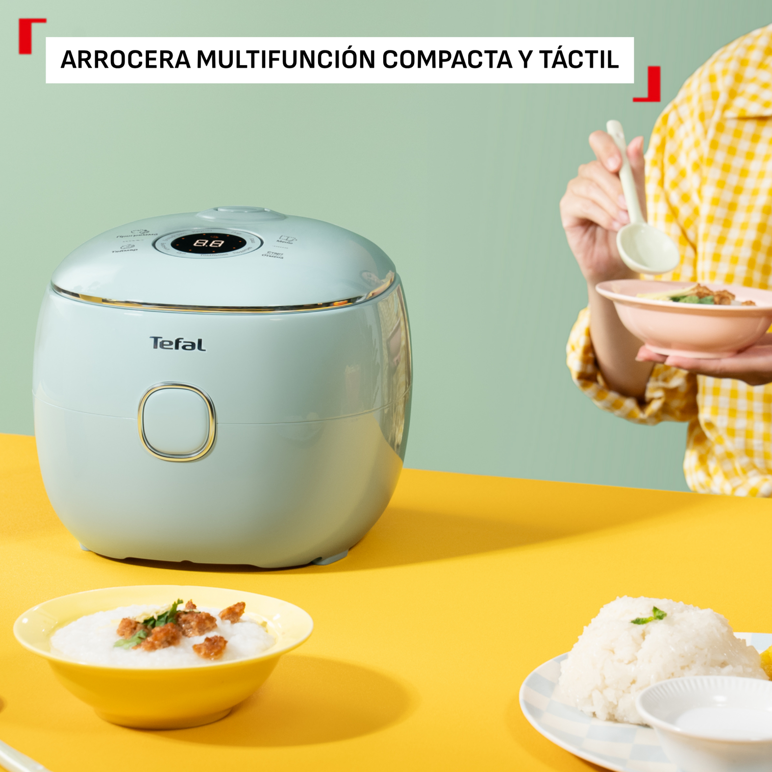 Una arrocera Tefal turquesa sobre una mesa amarilla con cuencos de arroz cerca.