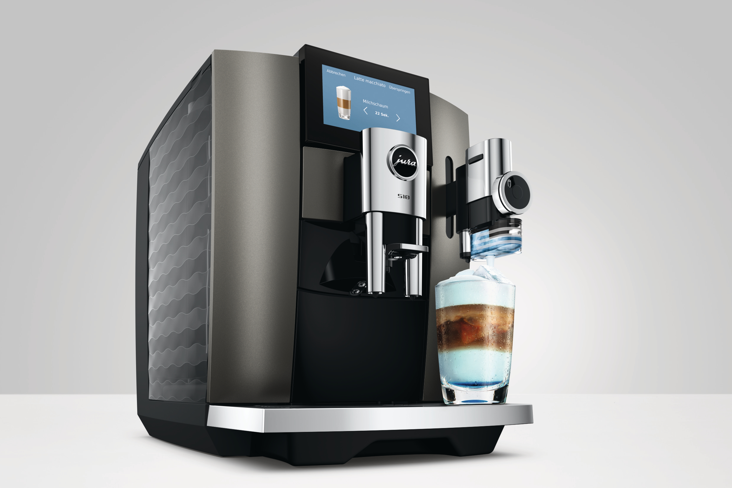 Moderne Jura S10 Kaffeemaschine auf weißem Tisch, bereitet ein Schichtgetränk in einem Glas zu.