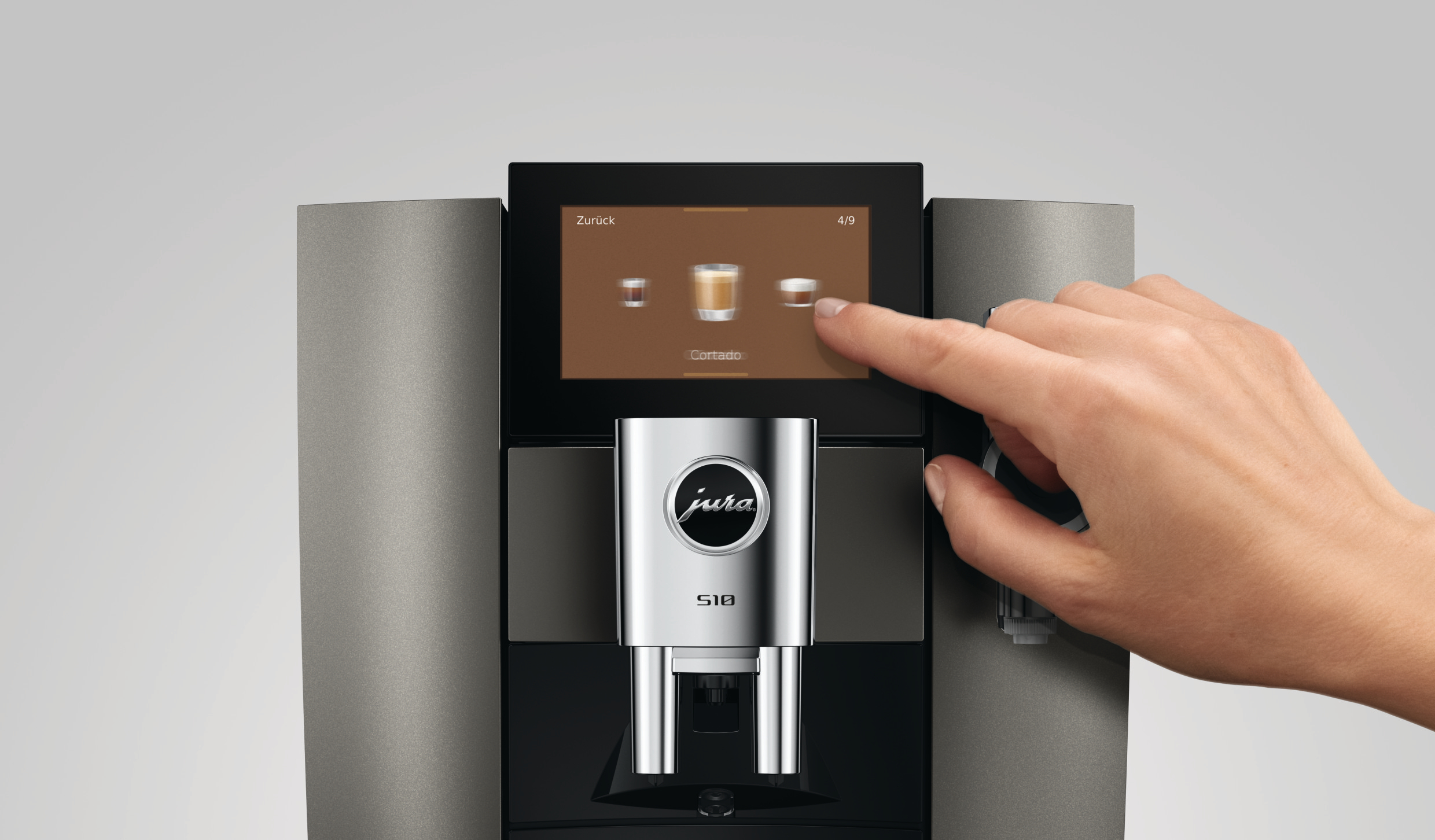 Eine Hand tippt auf den Touchscreen eines grauen Jura S10 Kaffeevollautomaten.