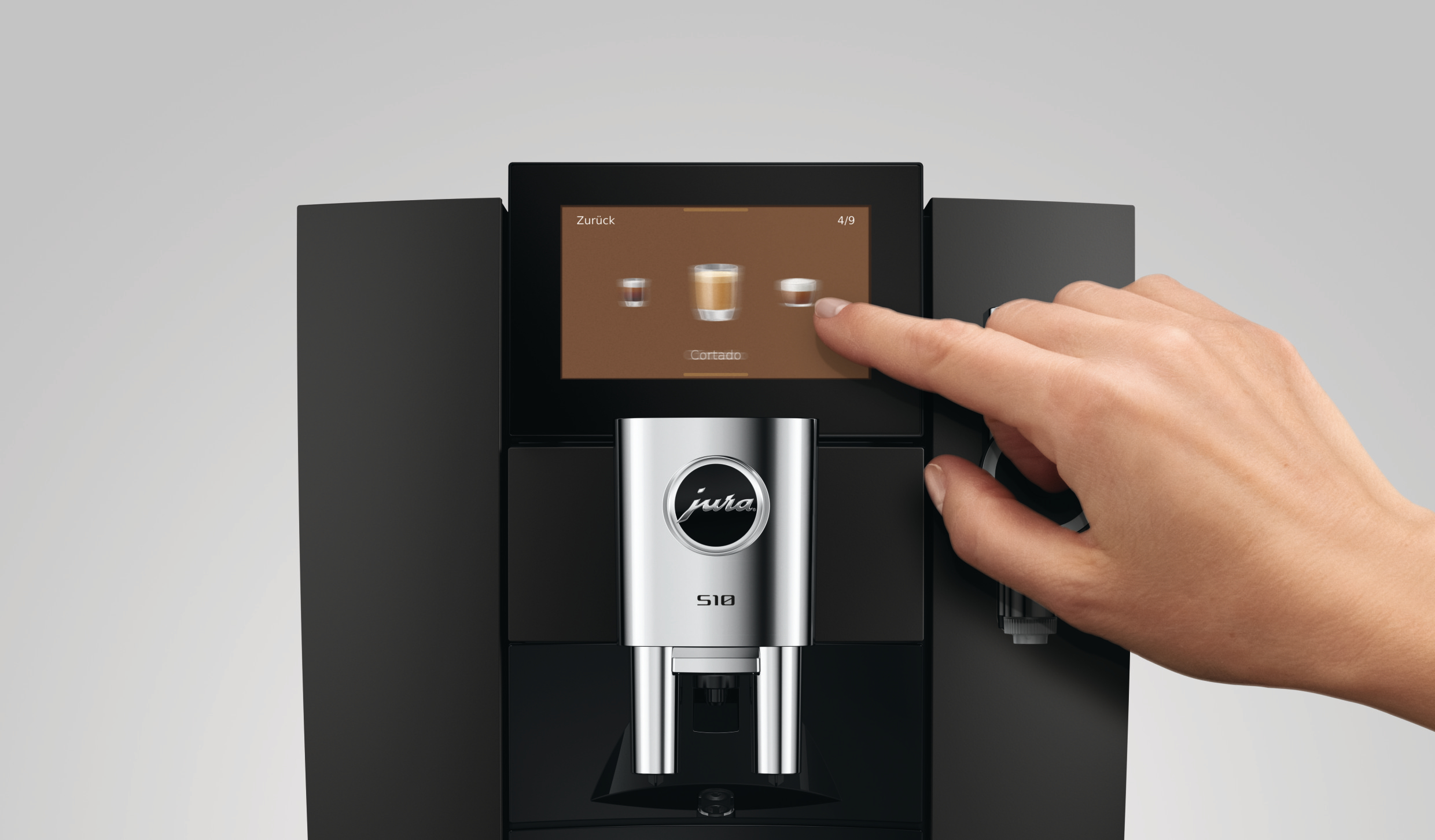Hand bedient den Touchscreen einer schwarzen Jura S10 Kaffeemaschine.