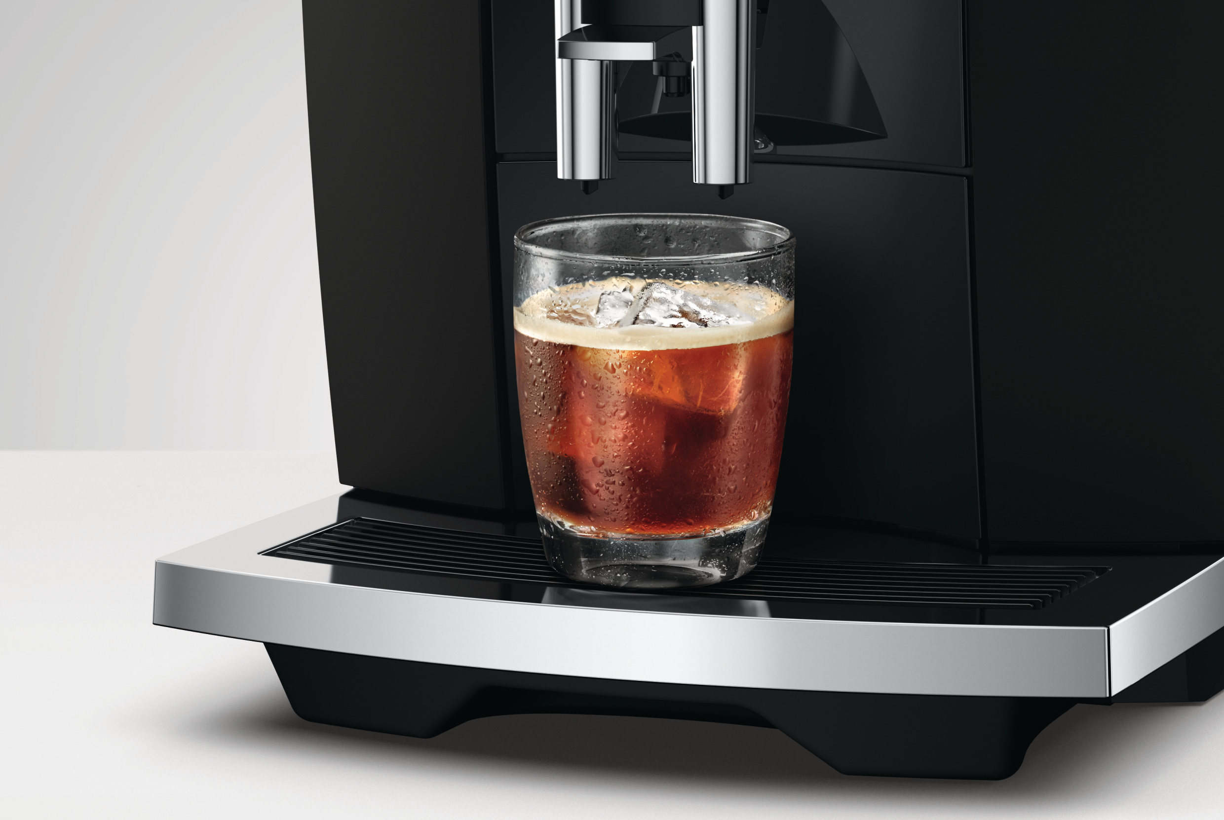 Ein Glas Eiskaffee mit Kondenswasser steht auf der Abtropfschale einer schwarzen Kaffeemaschine.