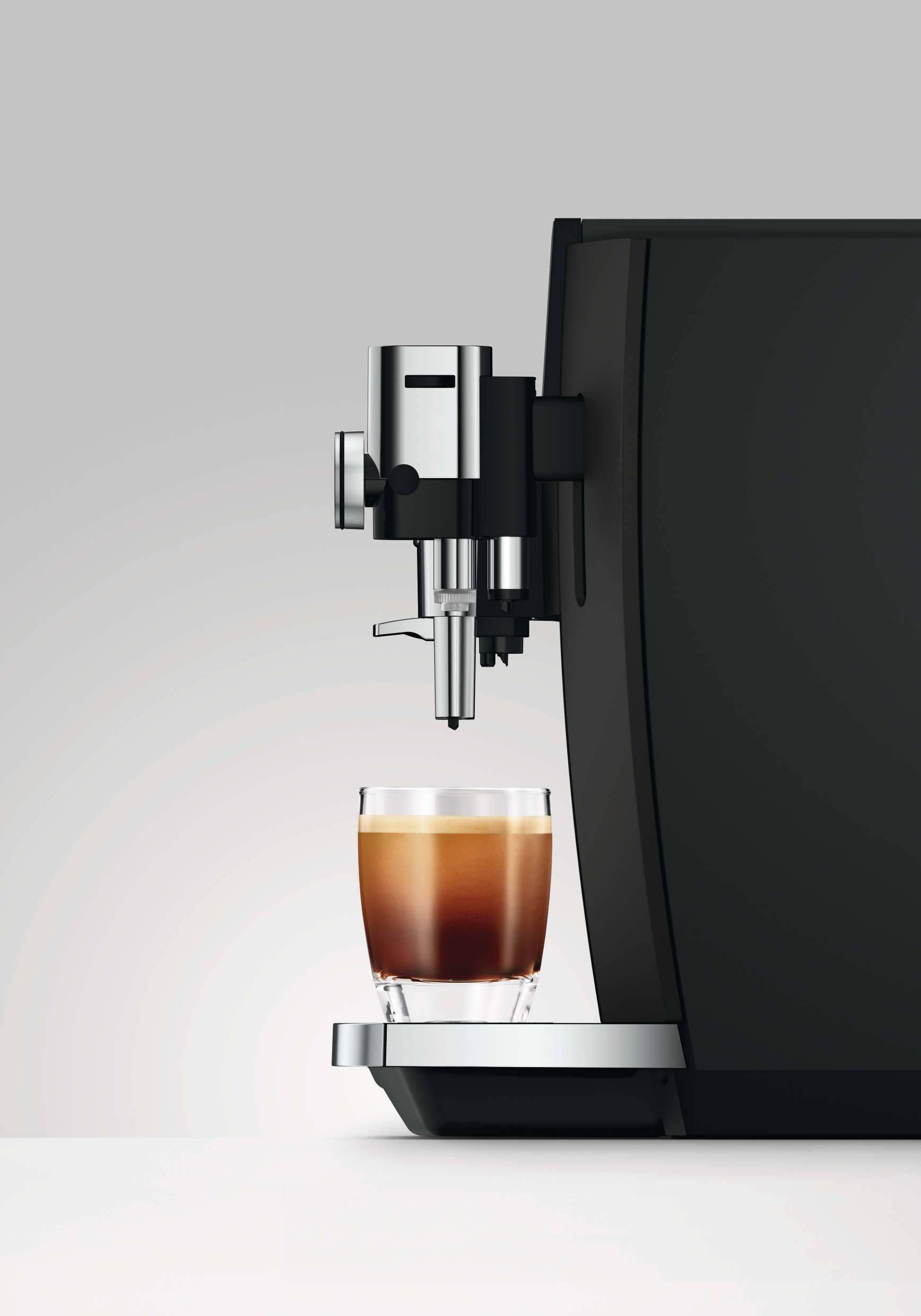 Moderne schwarze Kaffeemaschine mit Chromelementen und einer Glas Tasse Espresso auf einer silbernen Ablage.