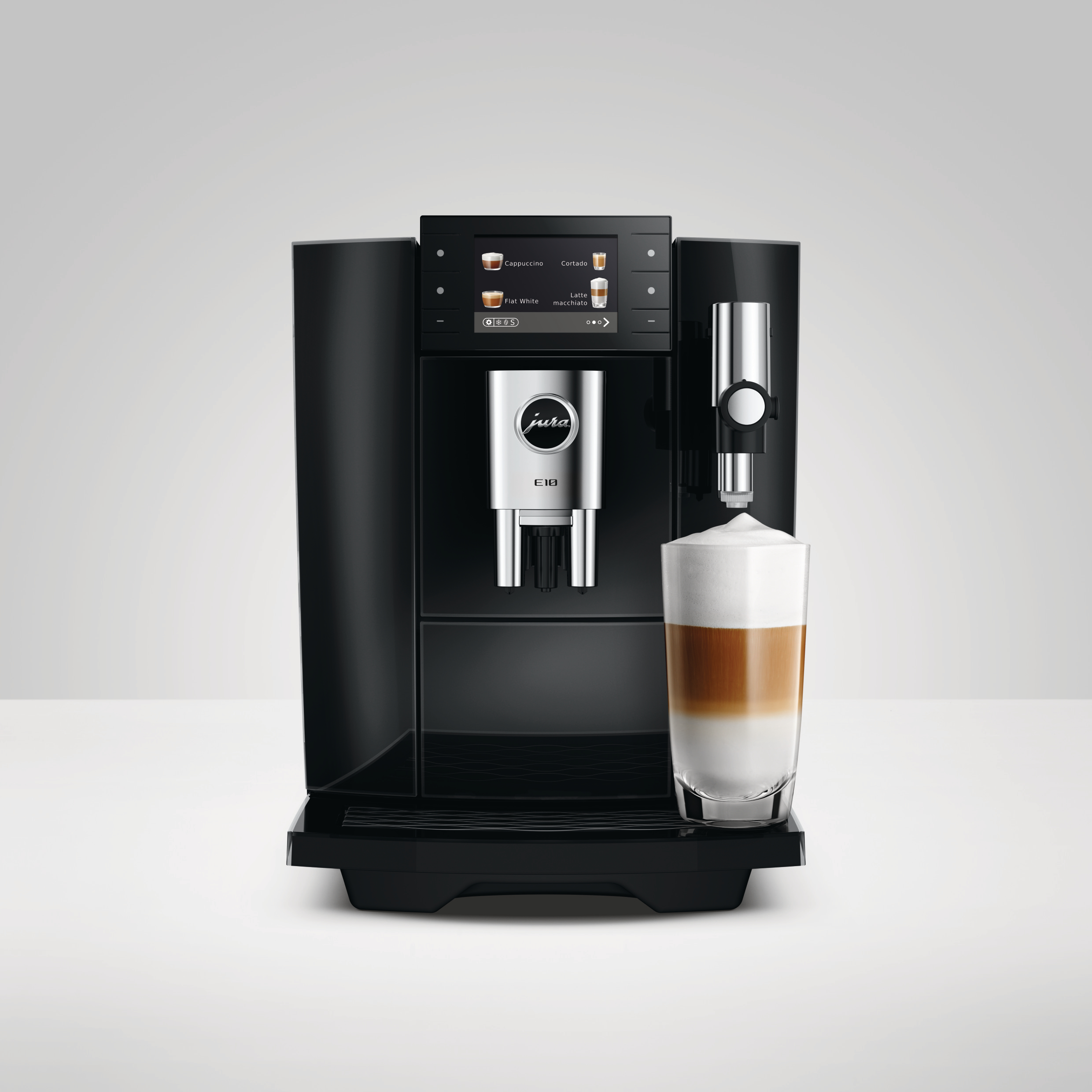Eine schwarze Jura E10 Kaffeemaschine mit Display giesst Schaum in ein Latte Macchiato Glas.