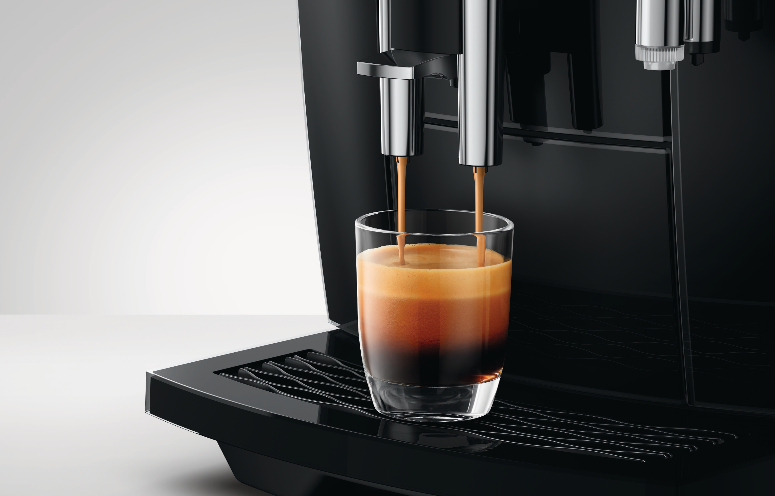 Ein schwarzer Kaffeevollautomat gießt frischen Espresso mit Crema in ein Glas auf der Abtropfschale.