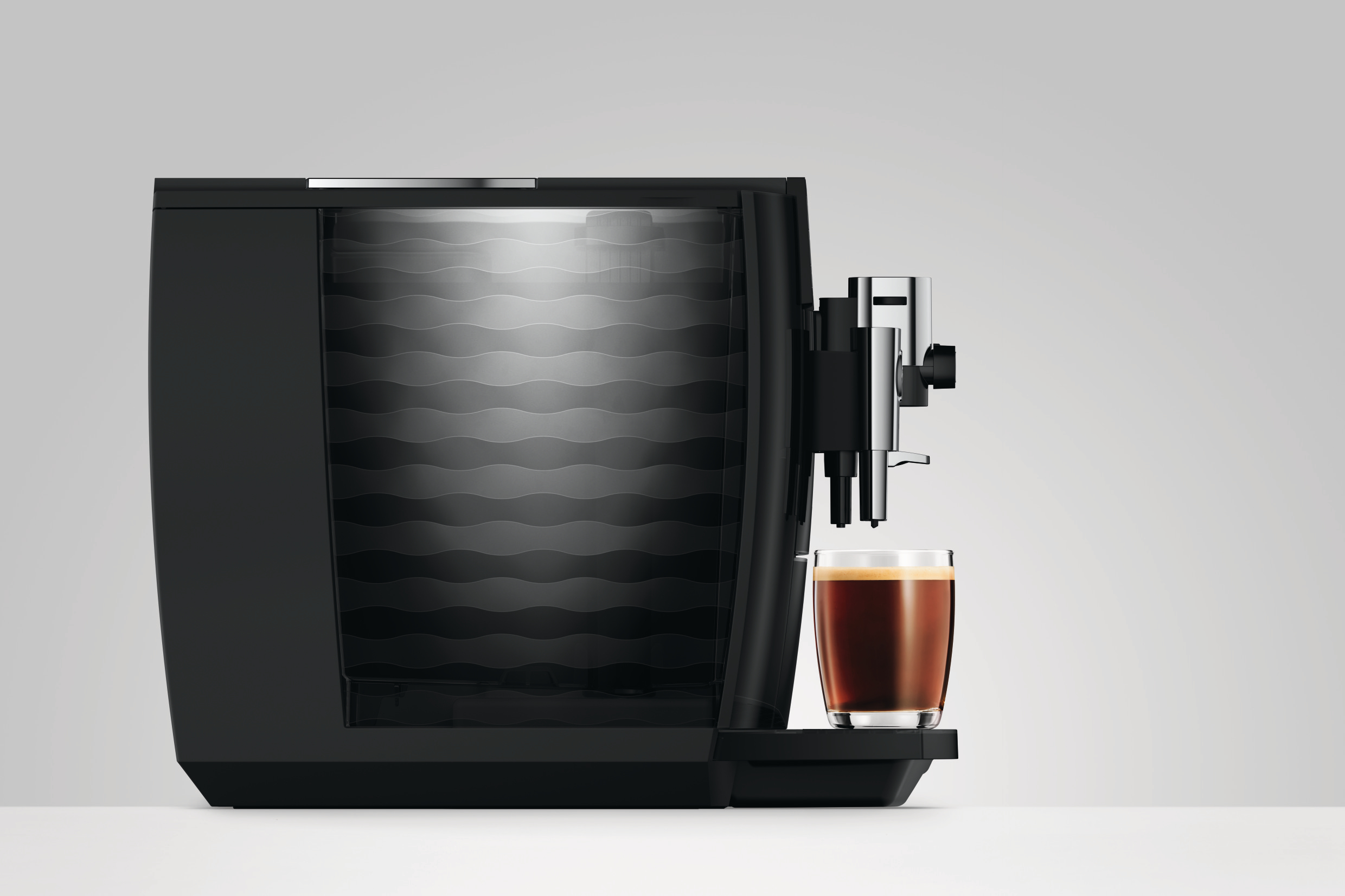 Eine schwarze moderne Kaffeemaschine mit einer Tasse Kaffee auf einem Tablett vor schlichtem Hintergrund.