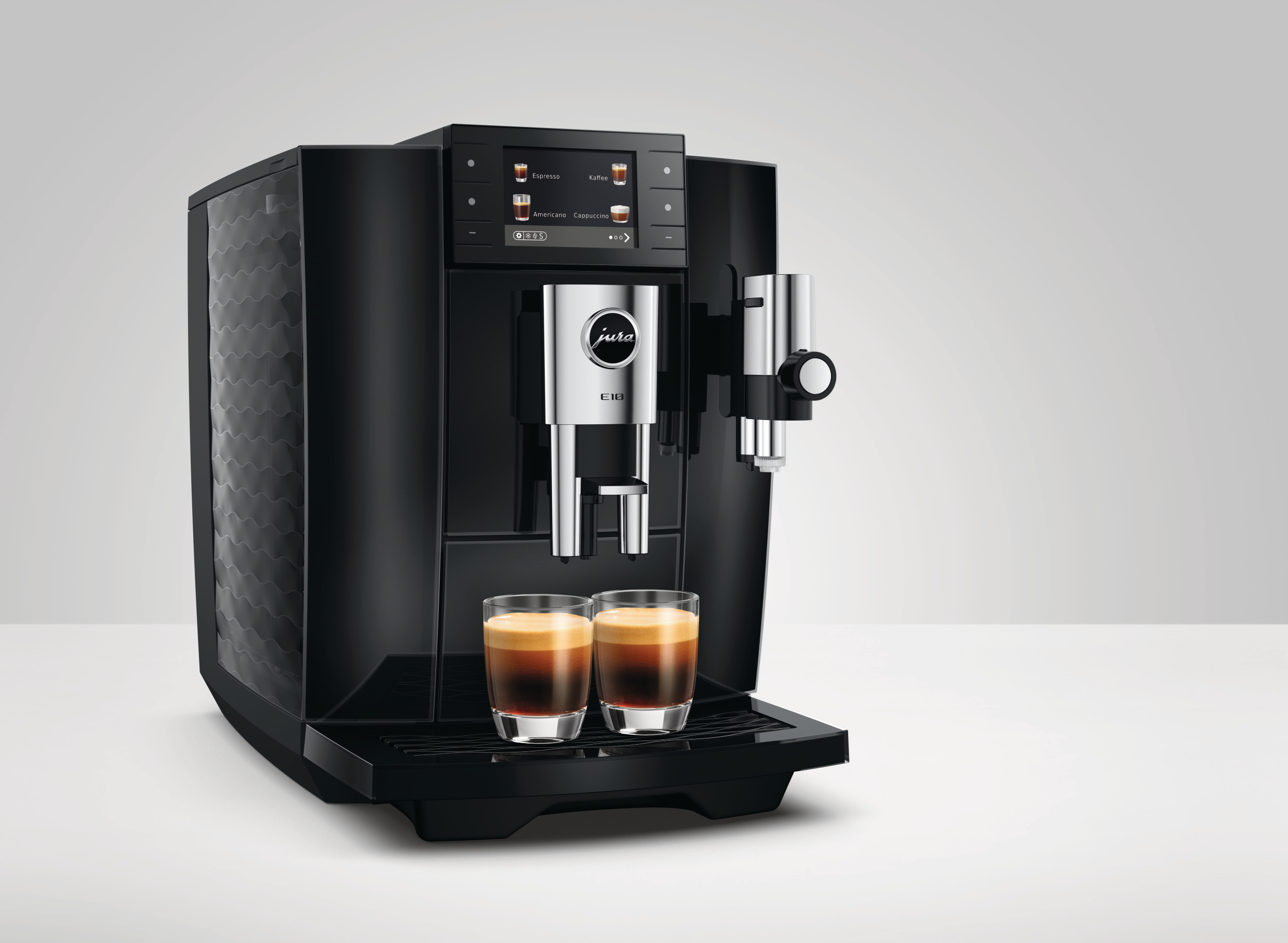 Eine schwarze Jura E10 Kaffeevollautomat steht auf einer weißen Oberfläche, davor zwei Gläser Espresso mit Crema.