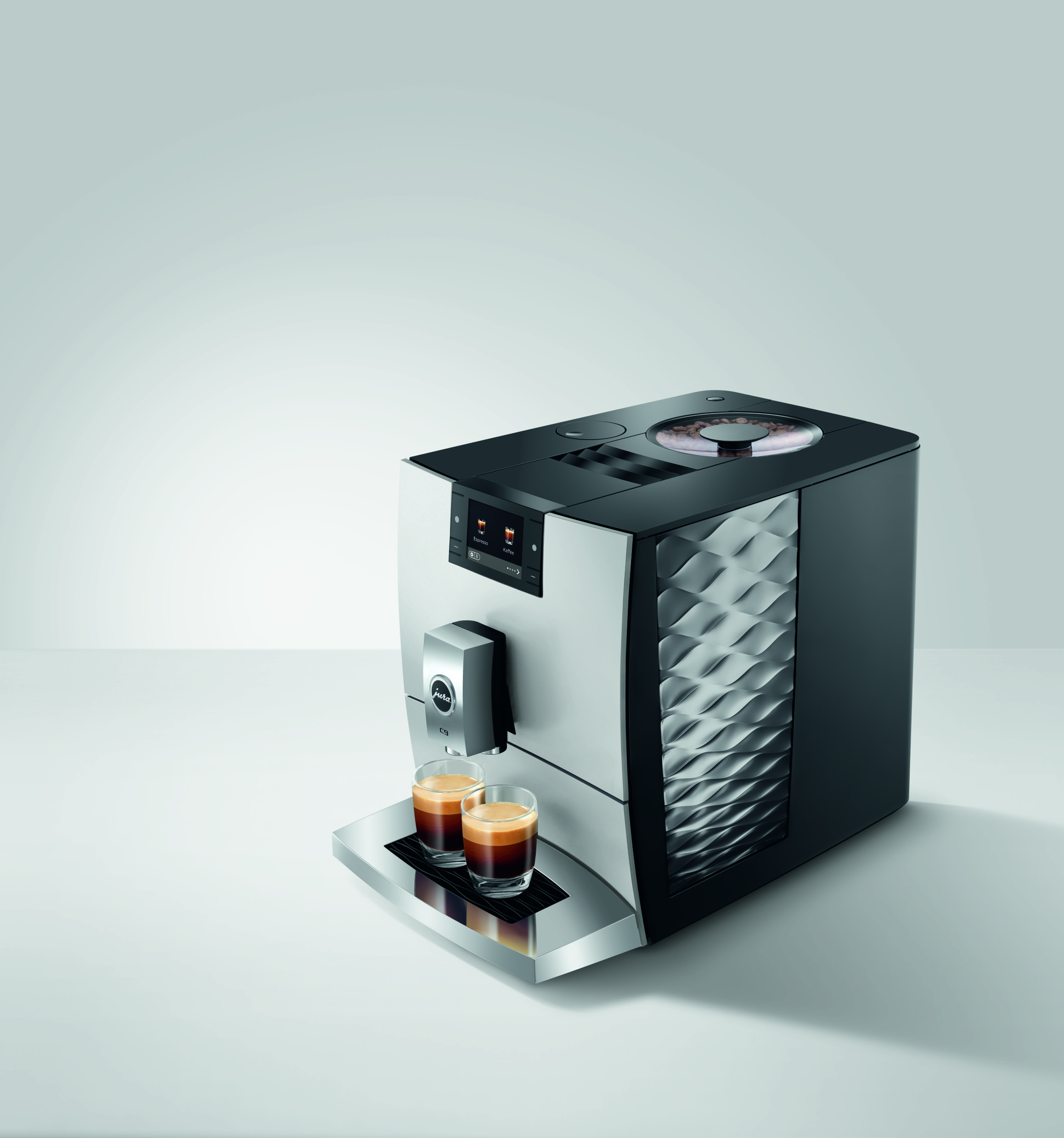 Moderne schwarz-silberne Kaffeemaschine mit zwei Espressotassen auf einer grauen Oberfläche vor weißem Hintergrund.
