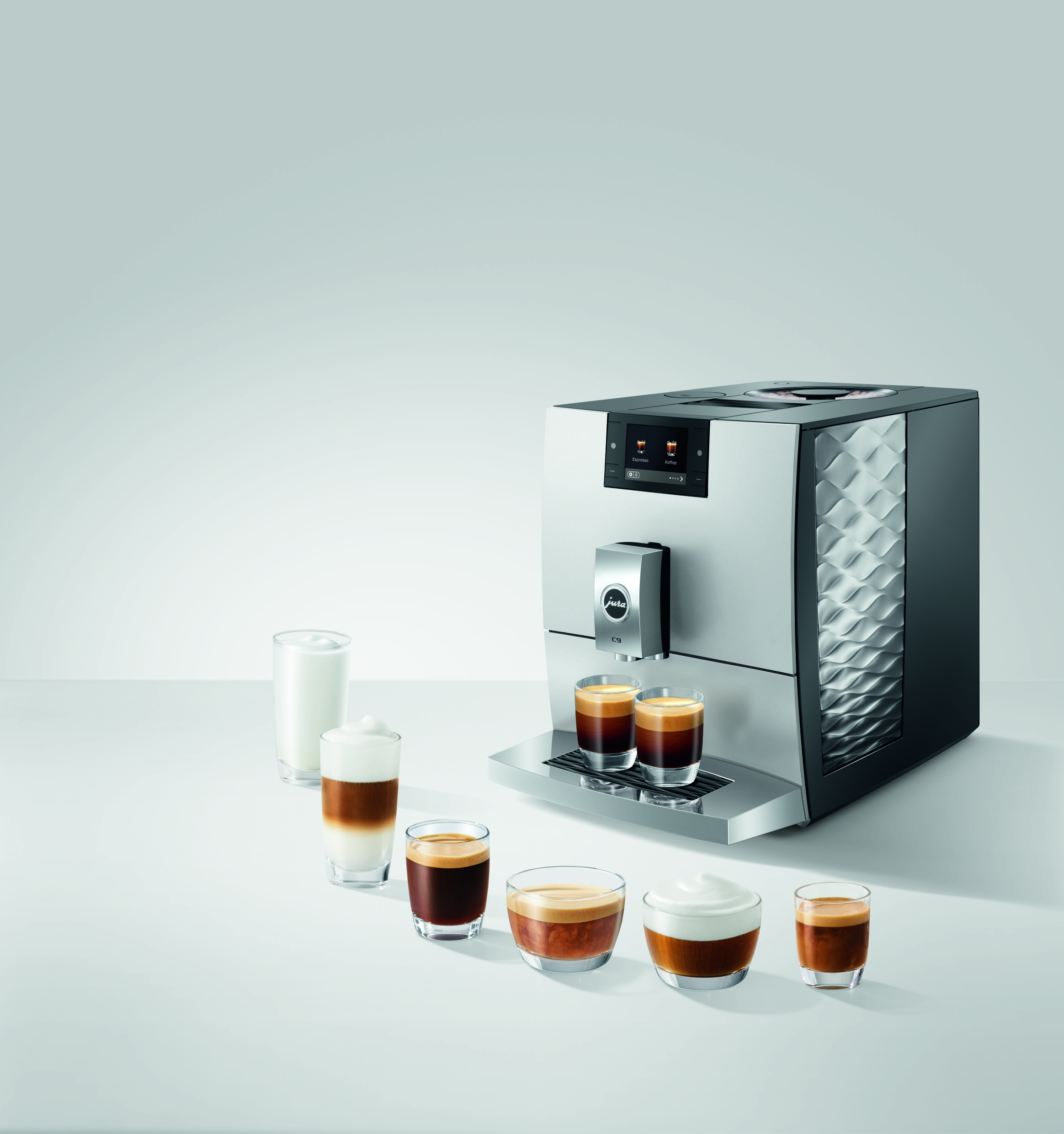 Moderne Jura Kaffeevollautomat mit verschiedenen Kaffeespezialitäten und Milch in Gläsern auf weißem Tisch.
