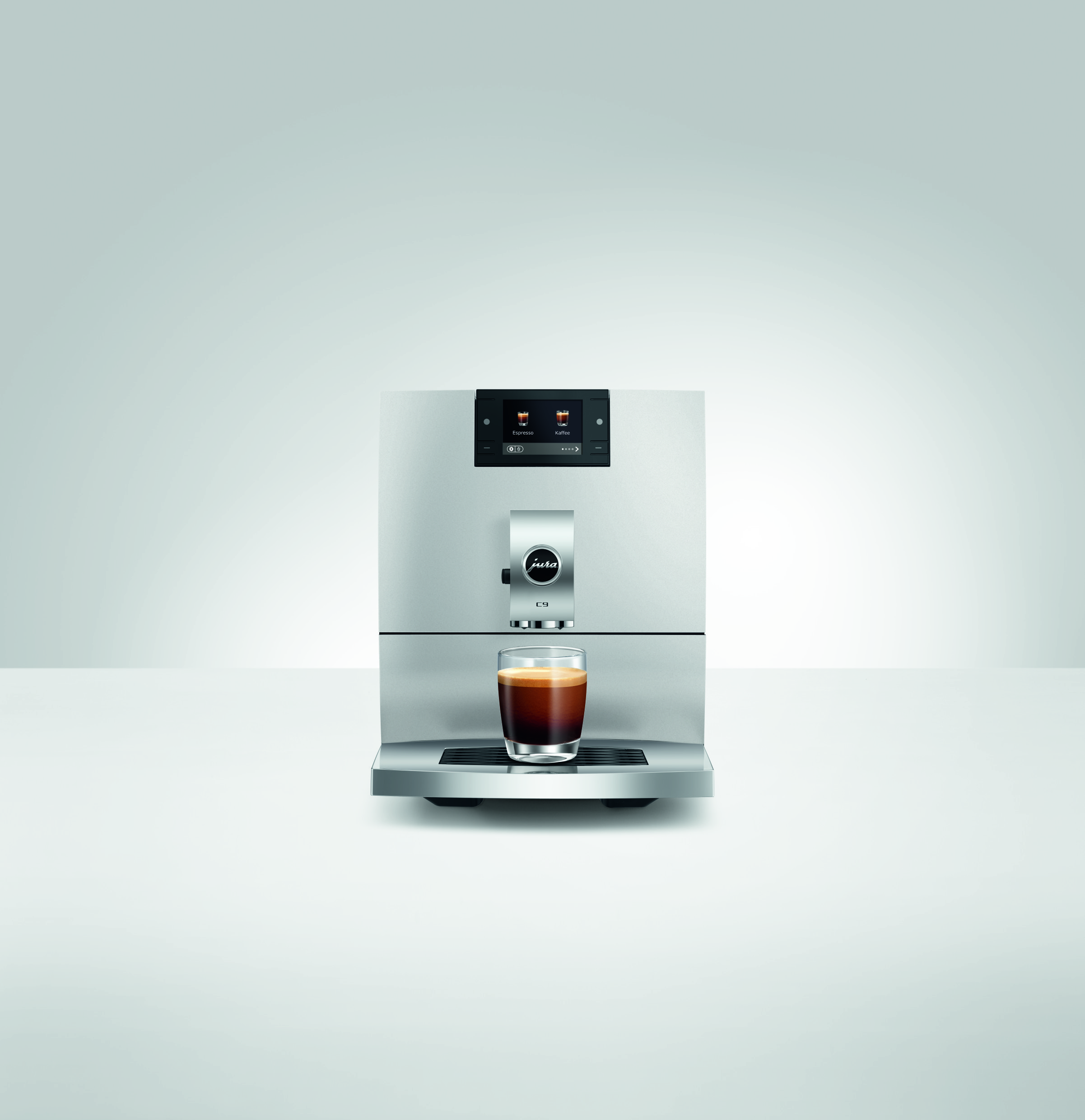 Moderne silberne Jura C9 Kaffeemaschine mit Display und einer Glas-Espressotasse auf der Abtropffläche.