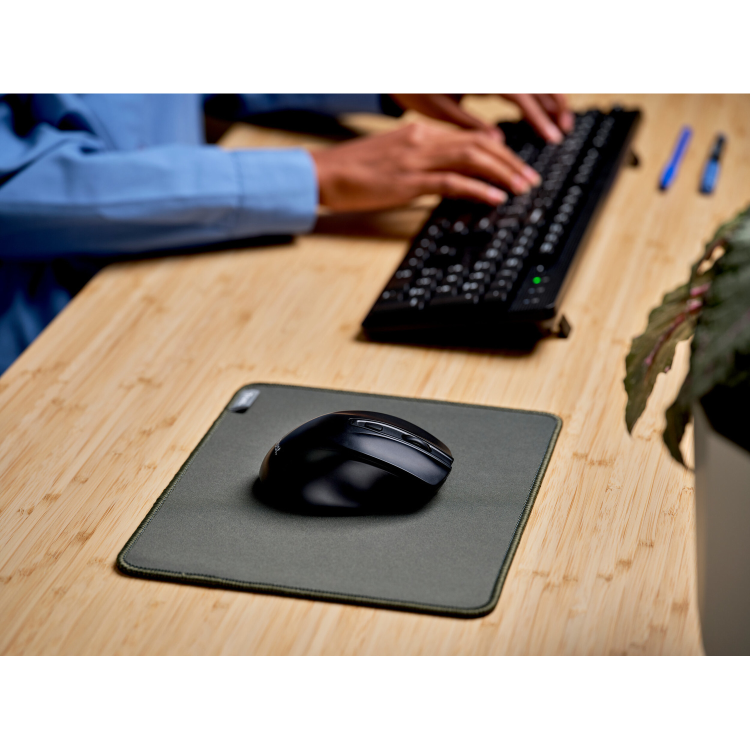 Un mouse per computer nero su un tappetino su una scrivania, mentre una persona digita sullo sfondo.