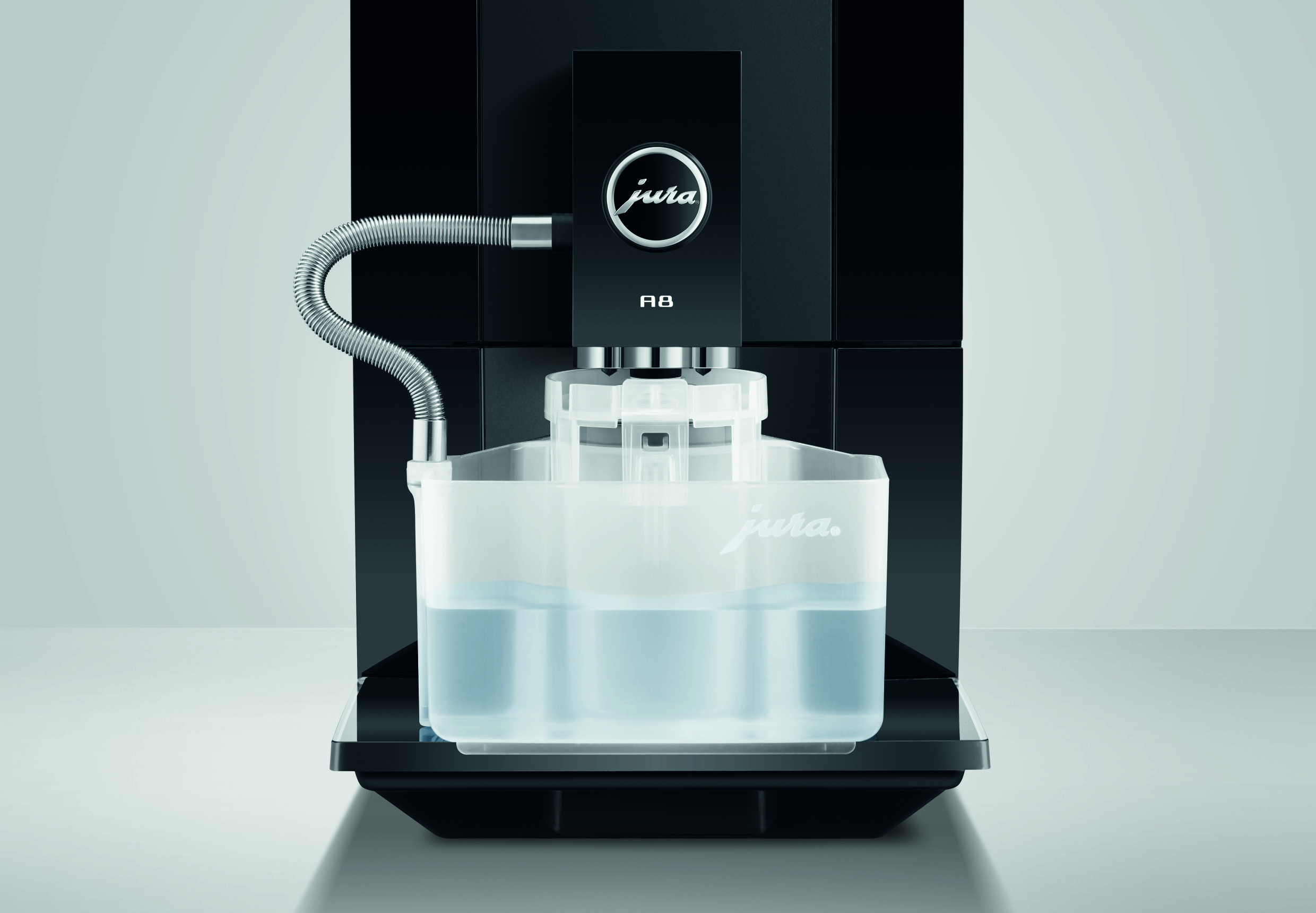 Schwarze Jura A8 Kaffeemaschine mit einem durchsichtigen Milchbehälter und einem silbernen Schlauch auf einer Ablage.