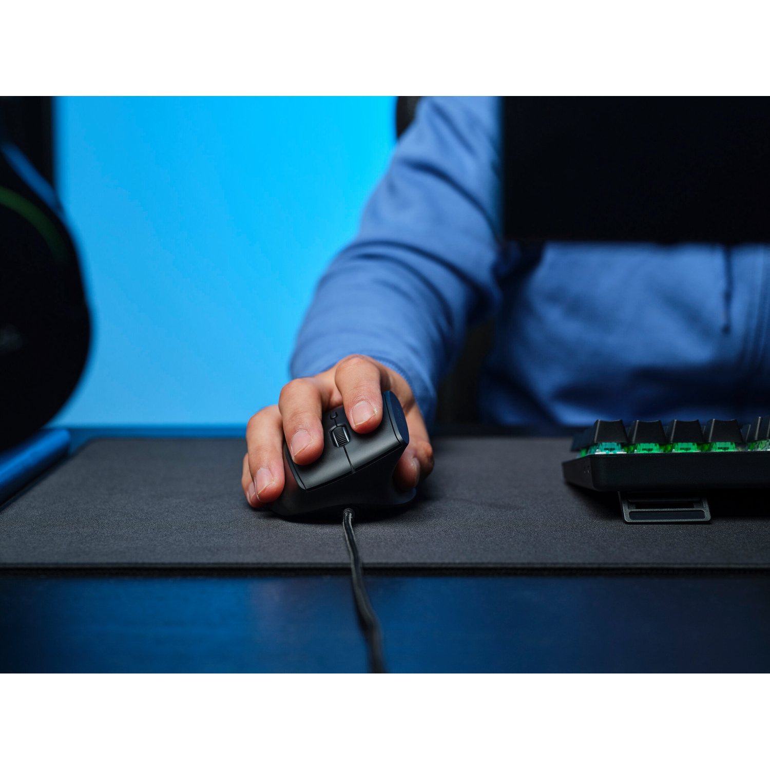 Una mano usa un mouse nero su un tappetino, con una tastiera a destra e sfondo blu.