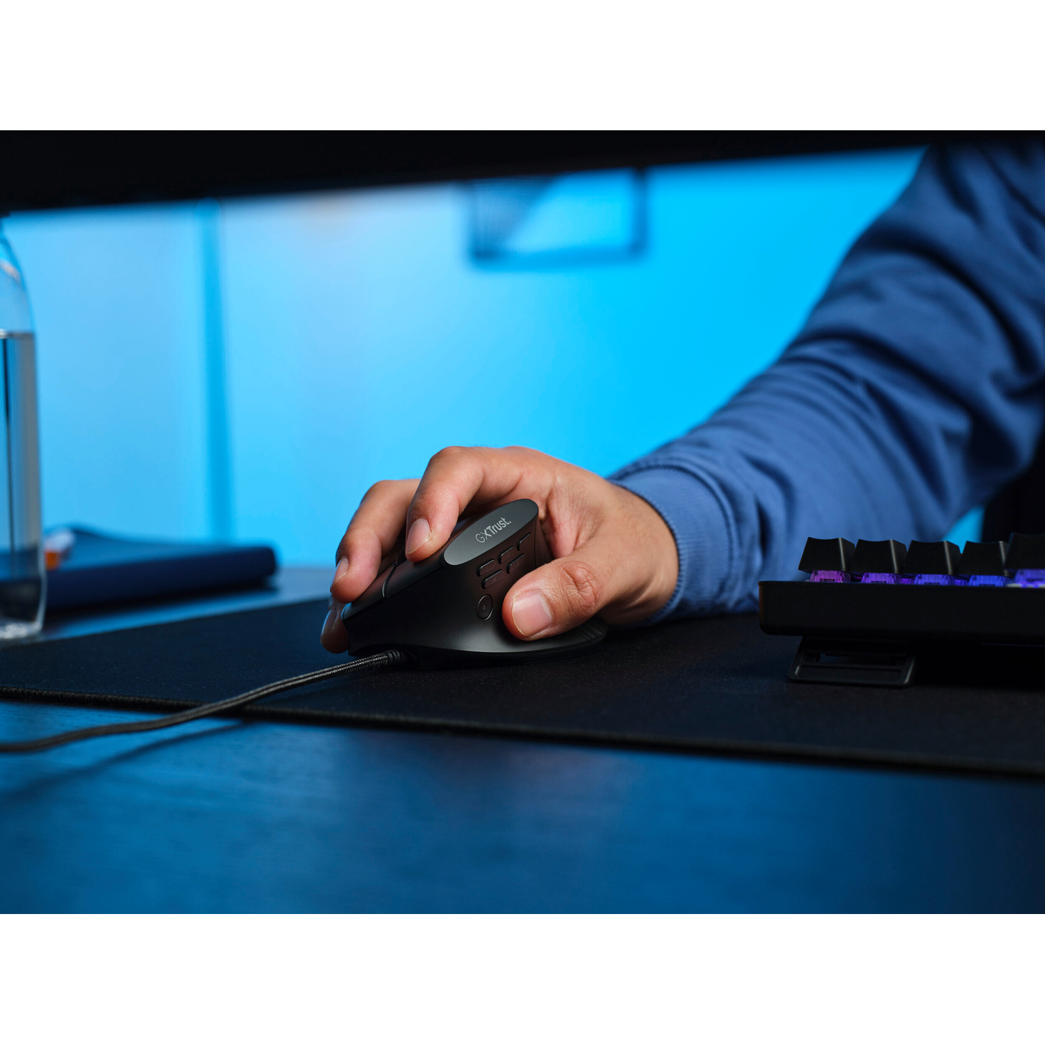 Una mano usa un mouse da gioco cablato nero su un tappetino davanti a una retroilluminazione blu.