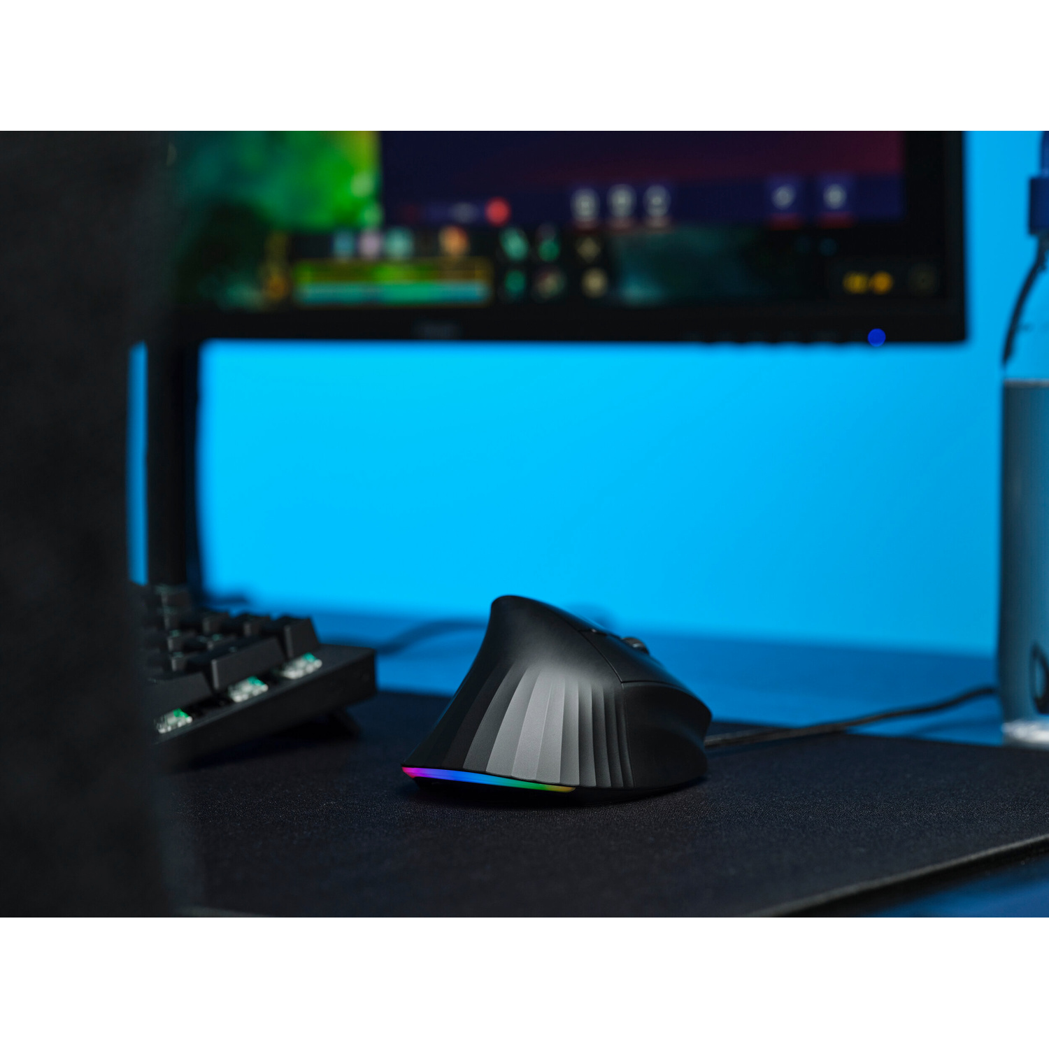 Un mouse ergonomico nero con illuminazione RGB su un tappetino davanti a un monitor.
