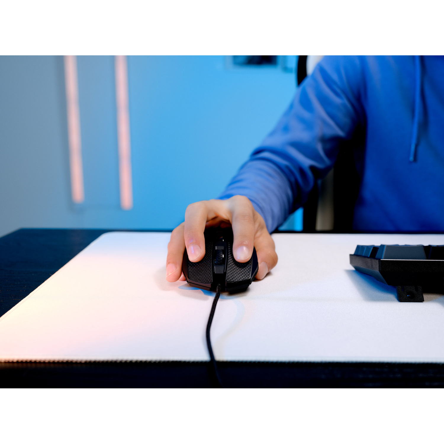 Persona con felpa blu usa un mouse da gioco nero su un tappetino bianco con sfondo blu.