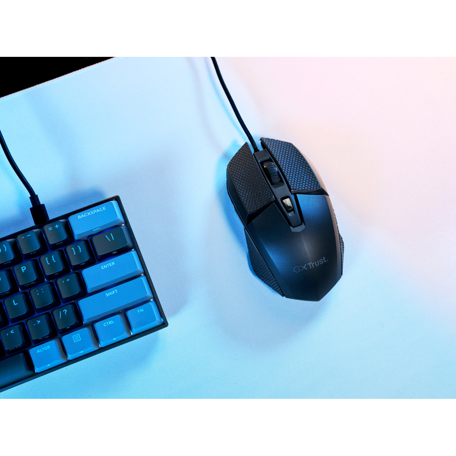 Un mouse da gioco nero GX Trust e una tastiera illuminata di blu su una superficie chiara.
