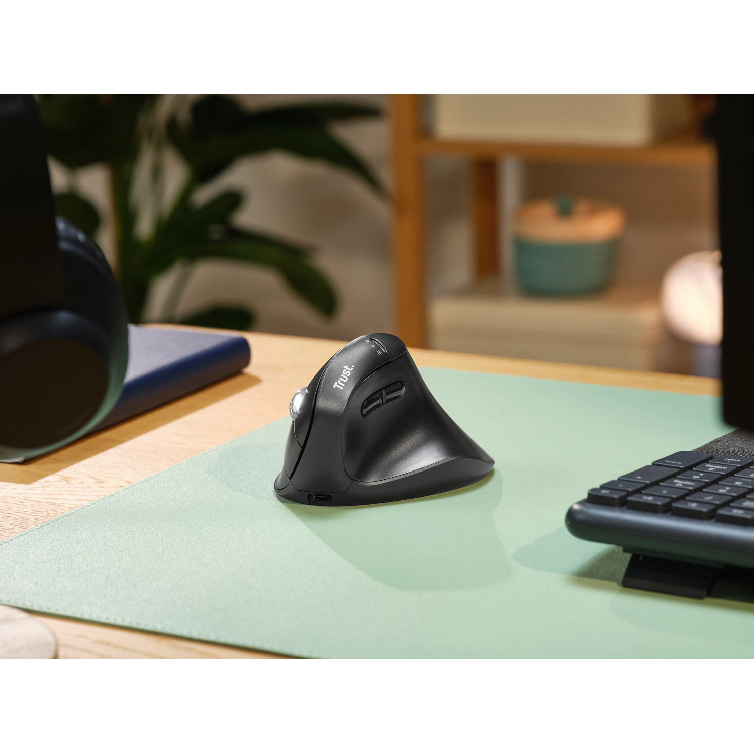 Un mouse verticale ergonomico nero su un tappetino da scrivania verde chiaro, circondato da tecnologia.
