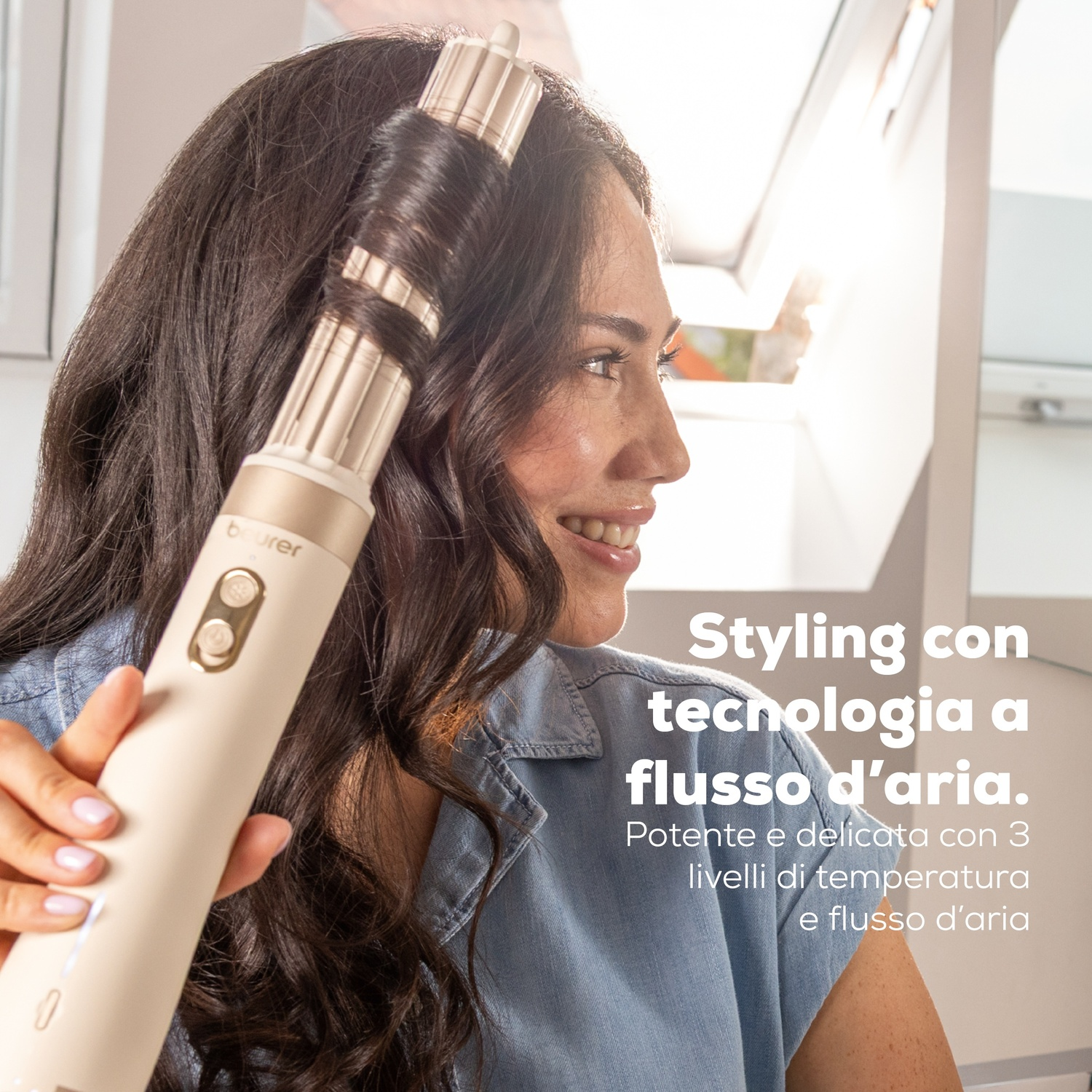 Una donna sorridente usa un styler ad aria beige sui suoi lunghi capelli scuri.