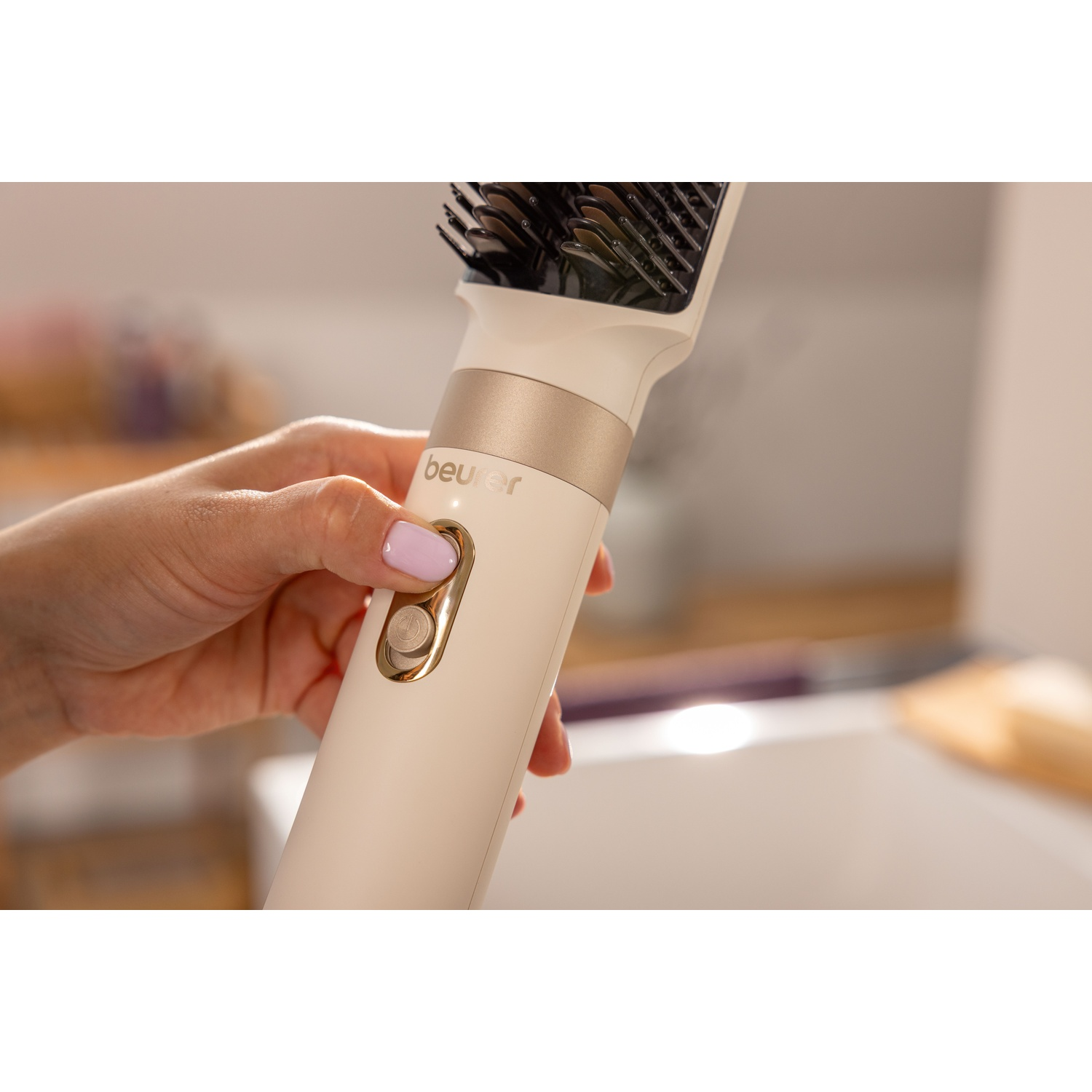 Una mano tiene un styler per capelli Beurer beige e preme il pulsante di accensione dorato.