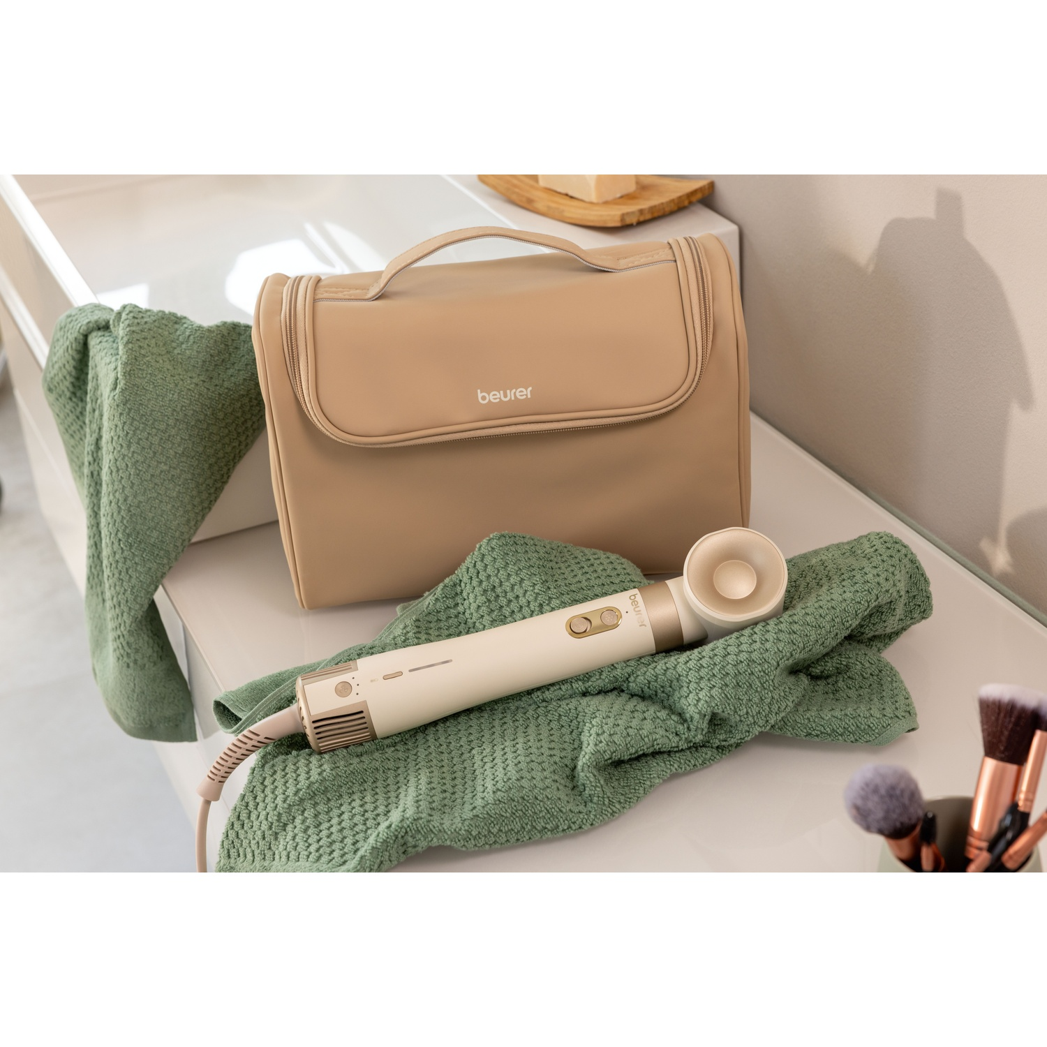 Borsa cosmetica beige e styler per capelli su asciugamani verdi in bagno.