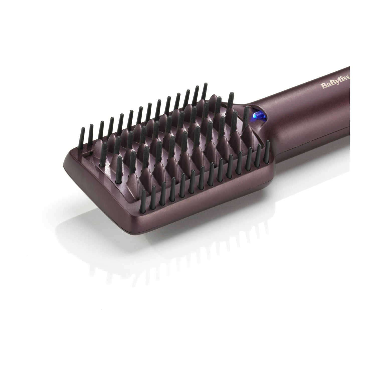 Una spazzola per capelli lisciante BaByliss viola con setole nere e un piccolo LED blu su superficie bianca.