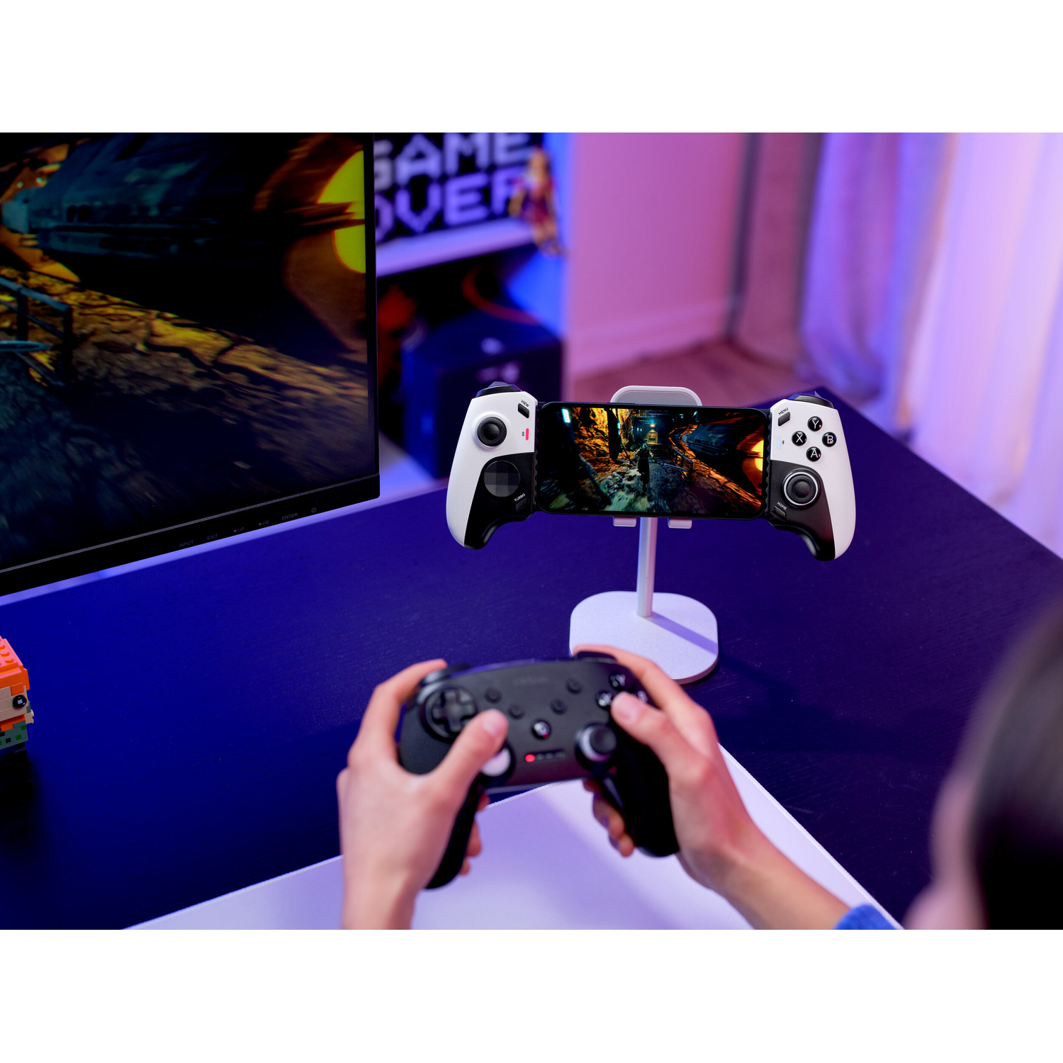 Una persona gioca con un controller nero mentre uno smartphone su un supporto ha un controller bianco.