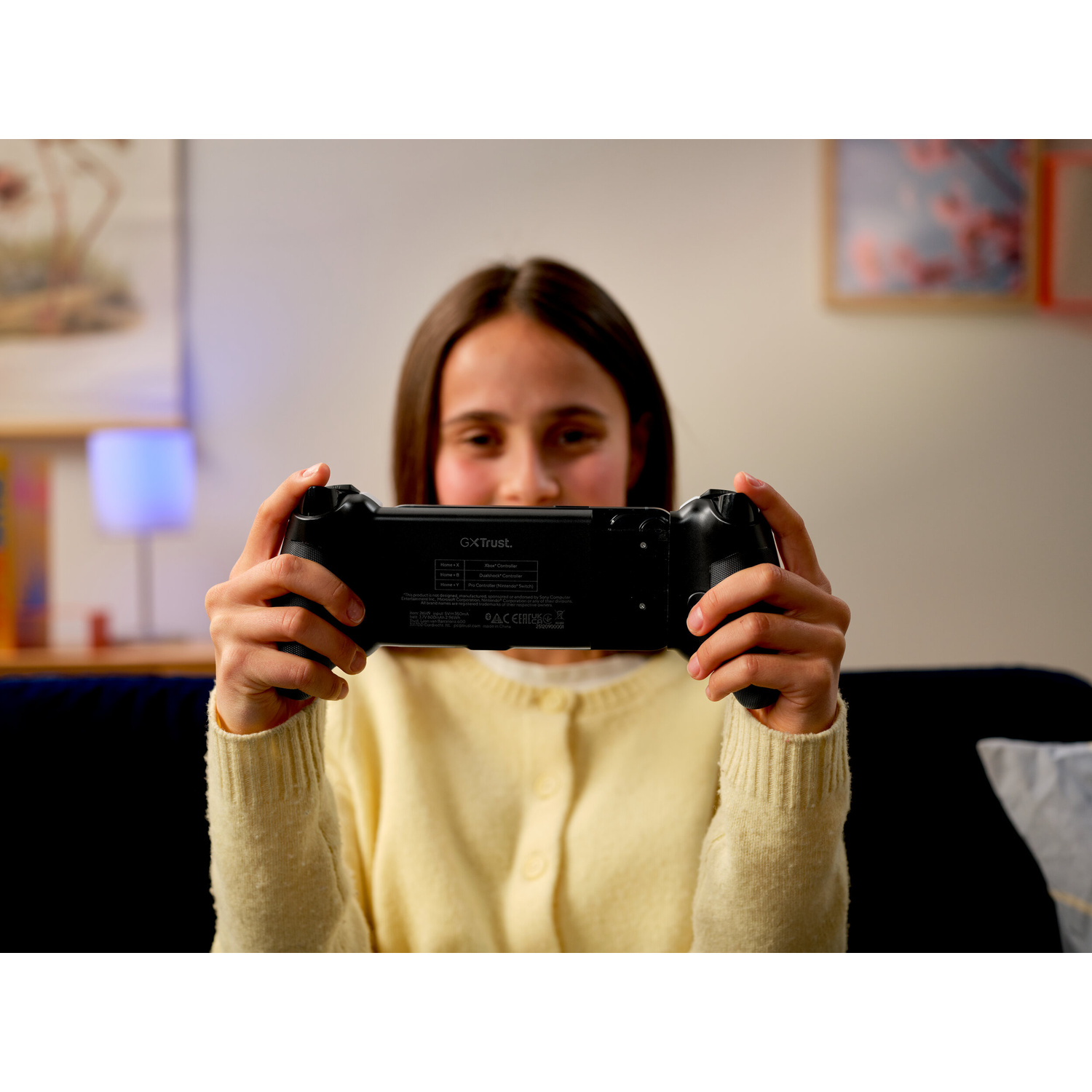 Una ragazza con un maglione giallo tiene in mano un controller nero.
