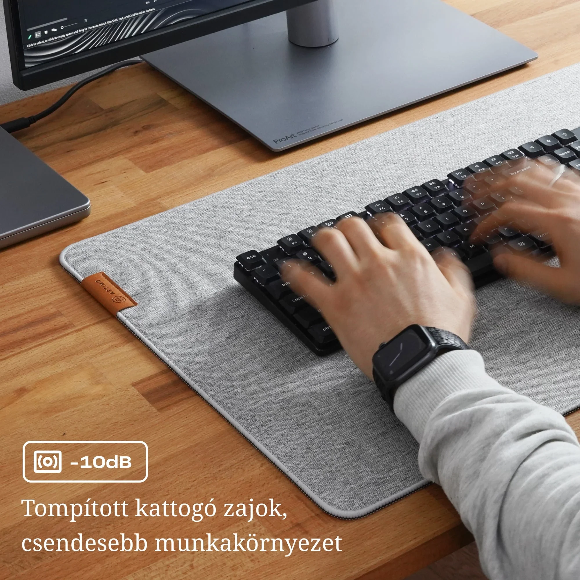 Kezek gyorsan gépelnek egy fekete billentyűzeten egy nagy szürke íróasztal-alátéten egy monitor előtt.