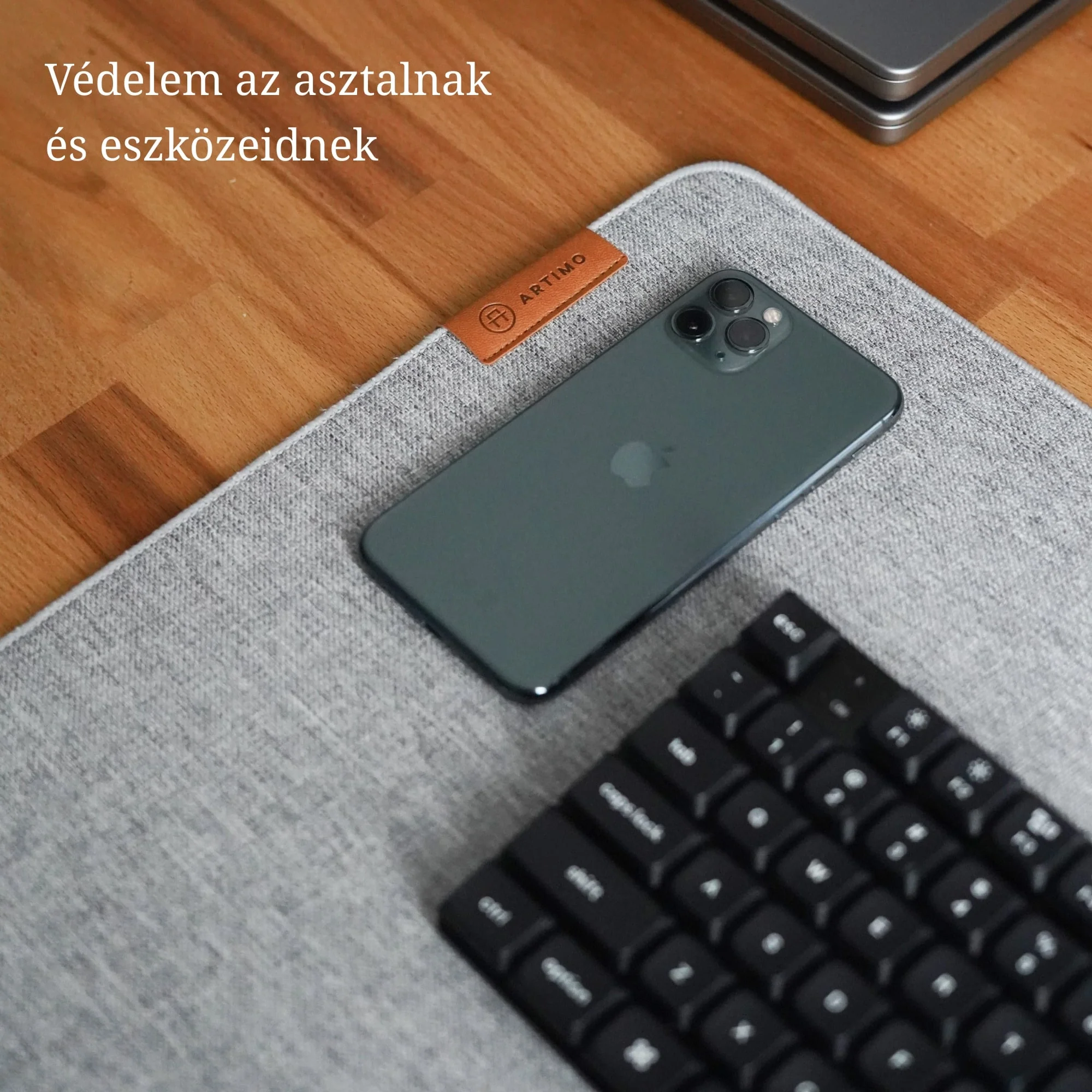 Okostelefon és billentyűzet szürke filc íróasztal alátéten, barna bőr címkével egy fa asztalon.
