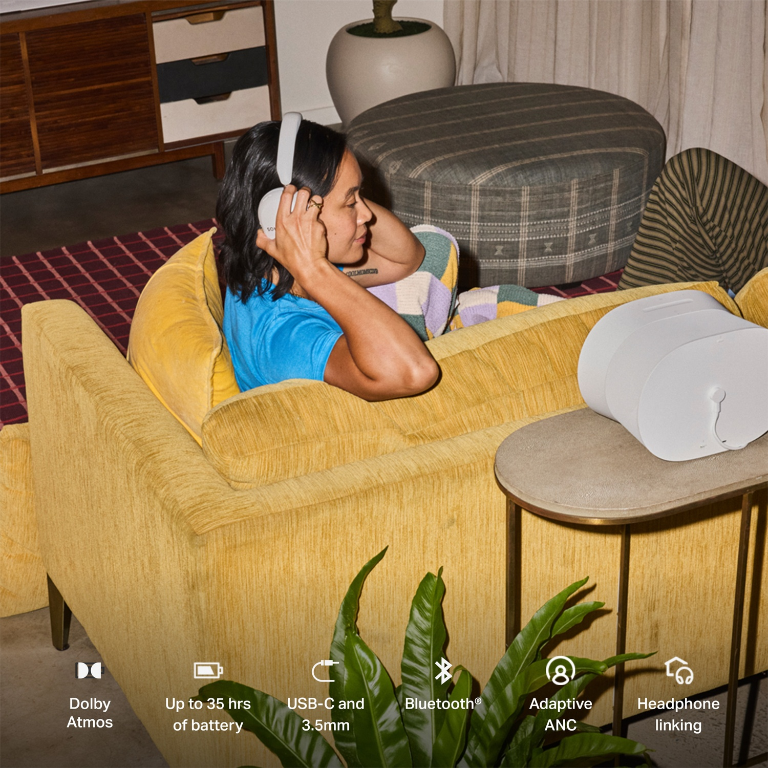 Een vrouw met een witte koptelefoon zit op een gele bank in een moderne woonkamer.