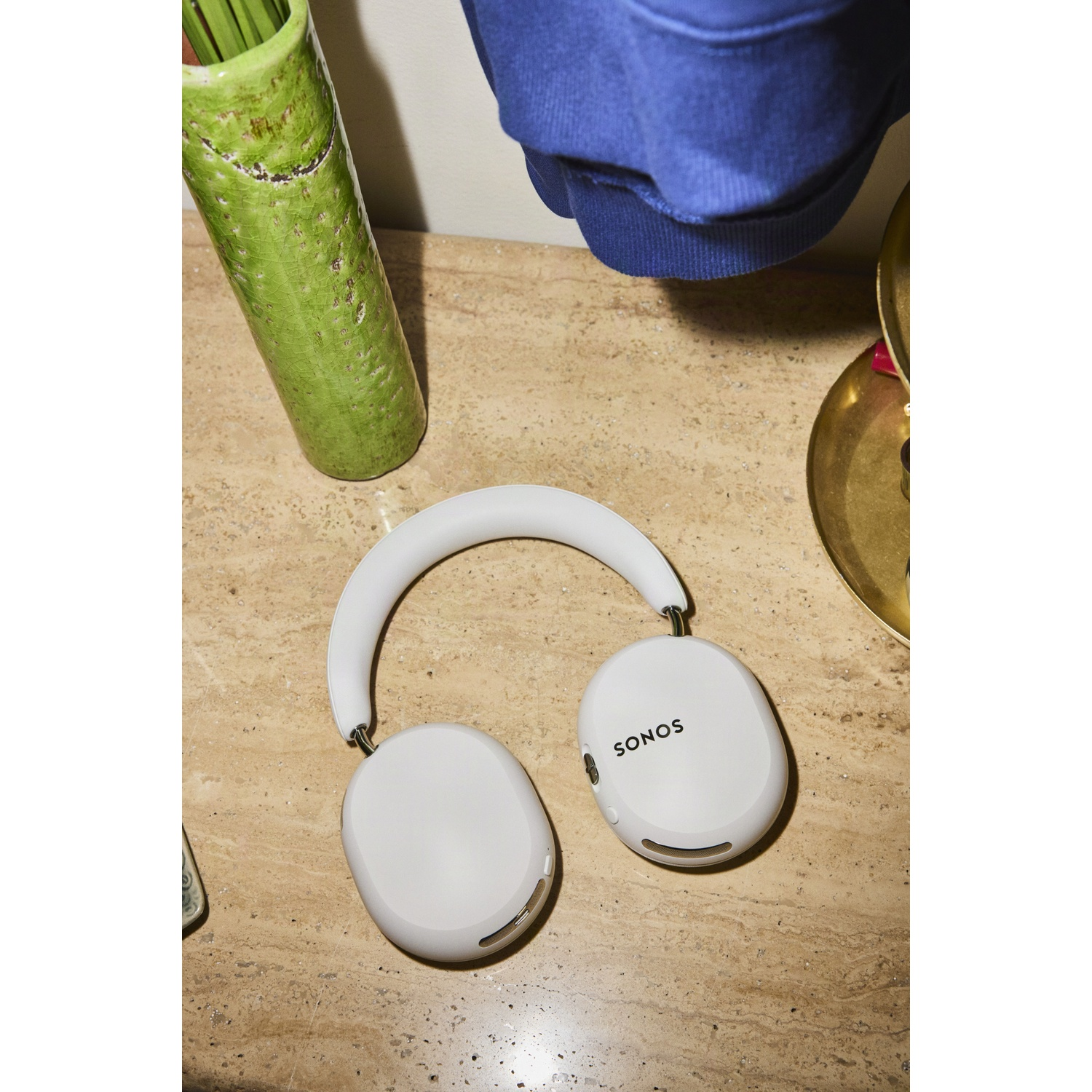Witte Sonos draadloze koptelefoon op een beige spikkelige tafel, naast een groene vaas en blauwe kleding.