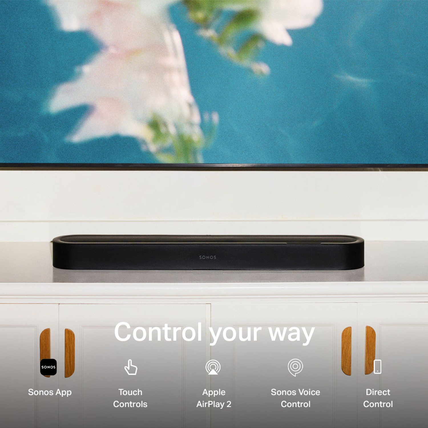 Une barre de son Sonos noire sur un meuble blanc sous un téléviseur, montrant des méthodes de contrôle.