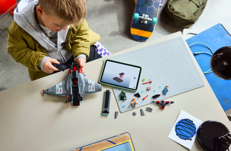 Ein Junge baut ein Lego-Flugzeug an einem Tisch mit Tablet, Figuren und einem Skateboard.