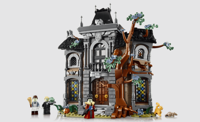 Lego-Geistervilla aus grauen Steinen, schwarzem Dach, kahlem Baum, vier Minifiguren, Katze und Ratte vor weißem Hintergrund.