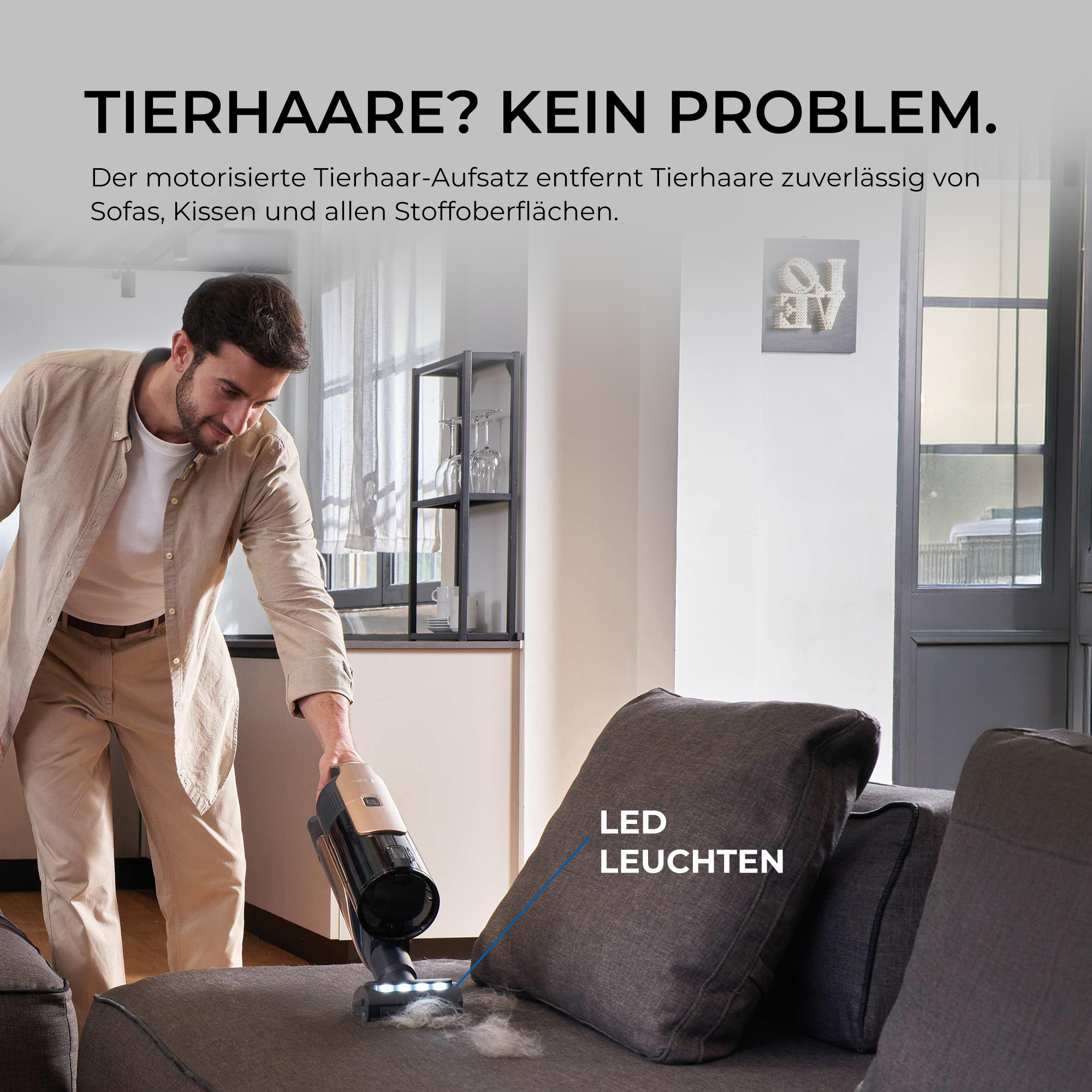 Ein Mann reinigt mit einem Handstaubsauger Tierhaare von einem grauen Sofa.