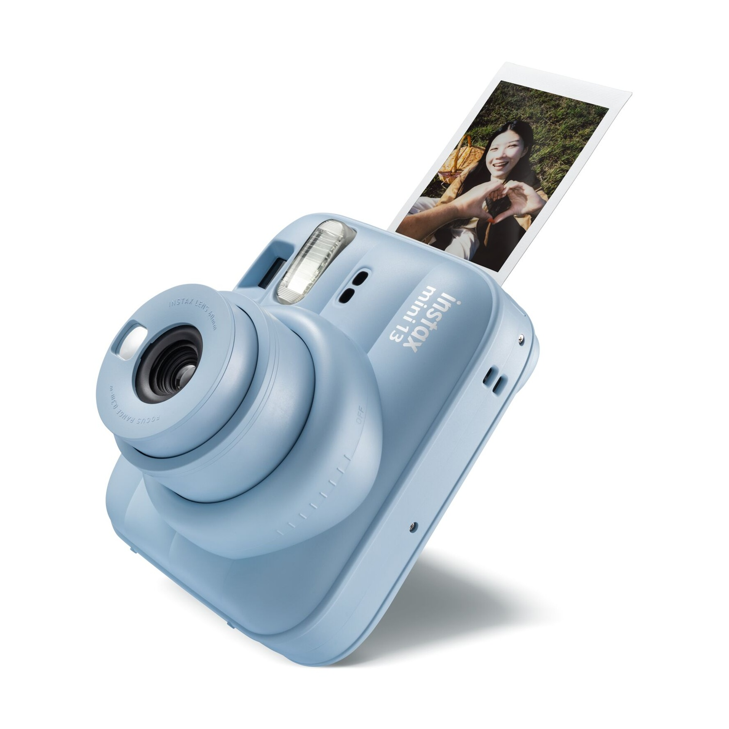 Fotocamera istantanea Instax Mini azzurra con una foto che mostra una donna sorridente che forma un cuore.