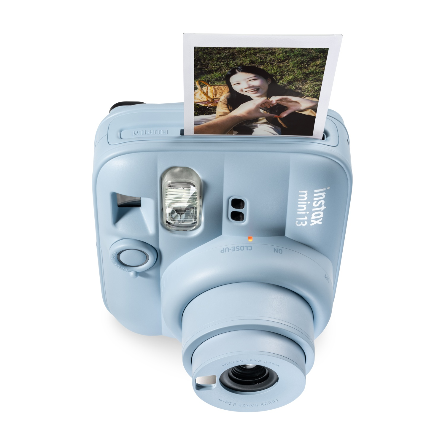 Fotocamera istantanea azzurra con la foto espulsa di una donna sorridente che fa un cuore.