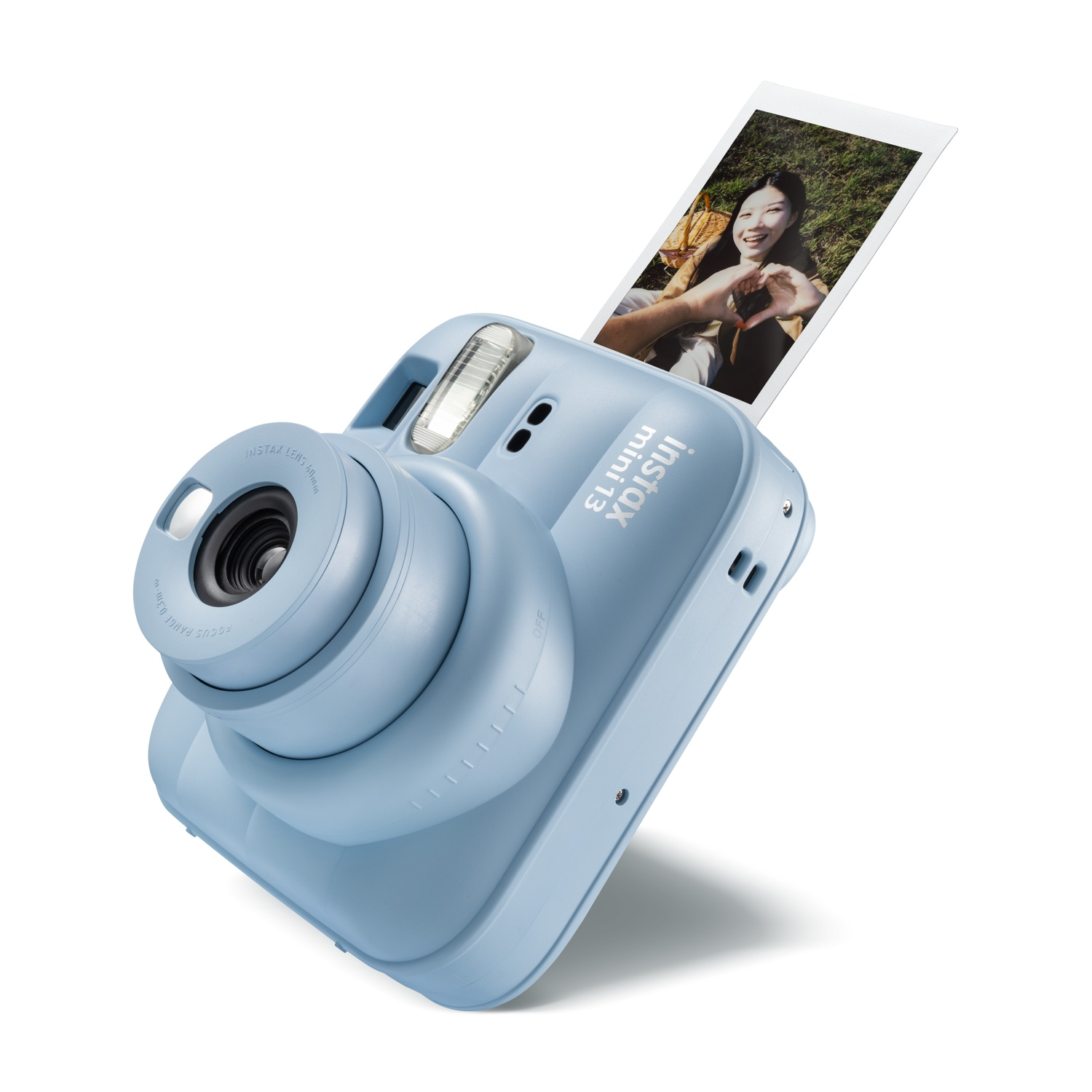 Fotocamera istantanea Instax Mini 13 azzurra con la foto di una donna sorridente che emerge dall'alto.